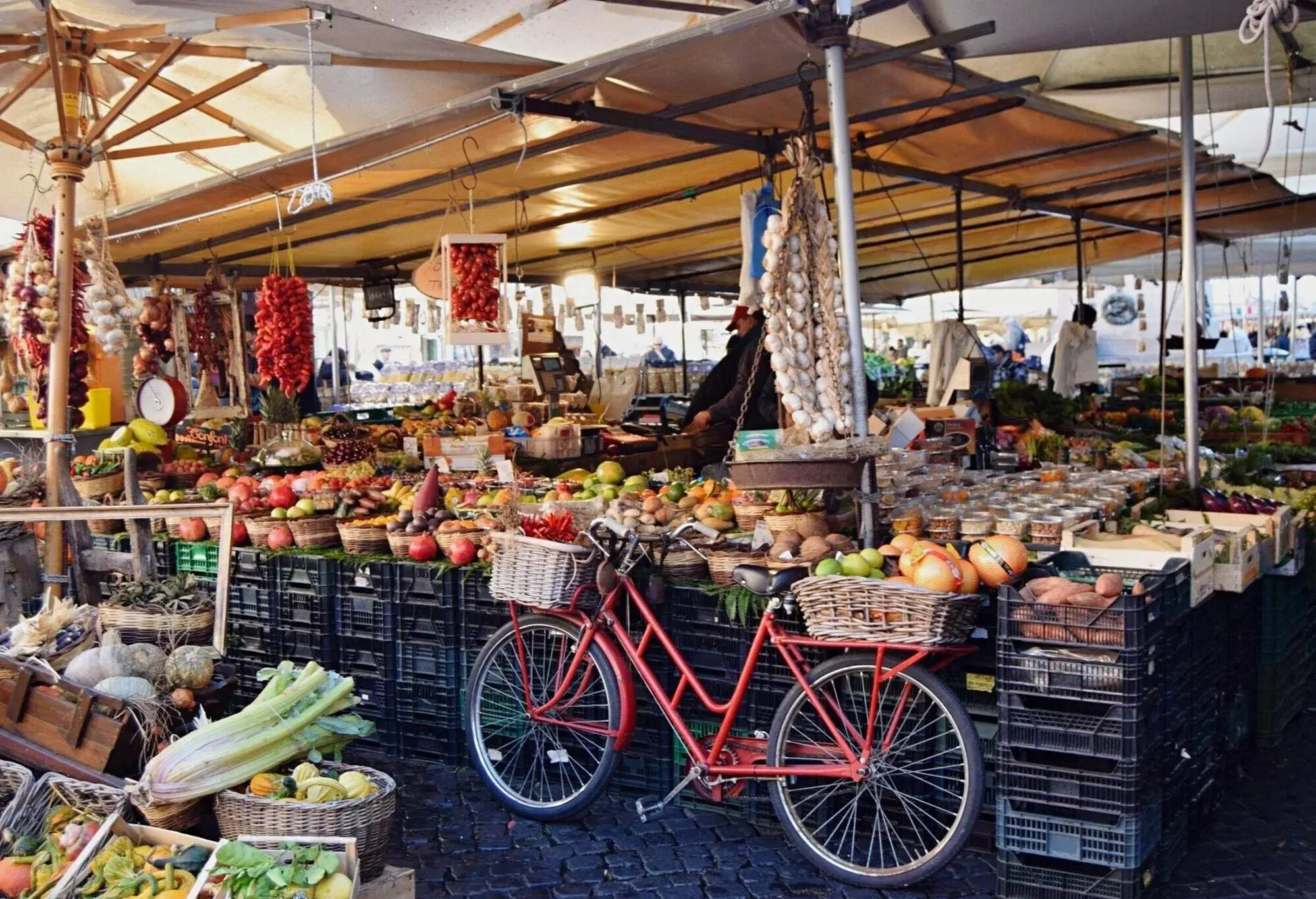 A tent with a display of assorted fruits for sale beside a bicycle with baskets full of products.