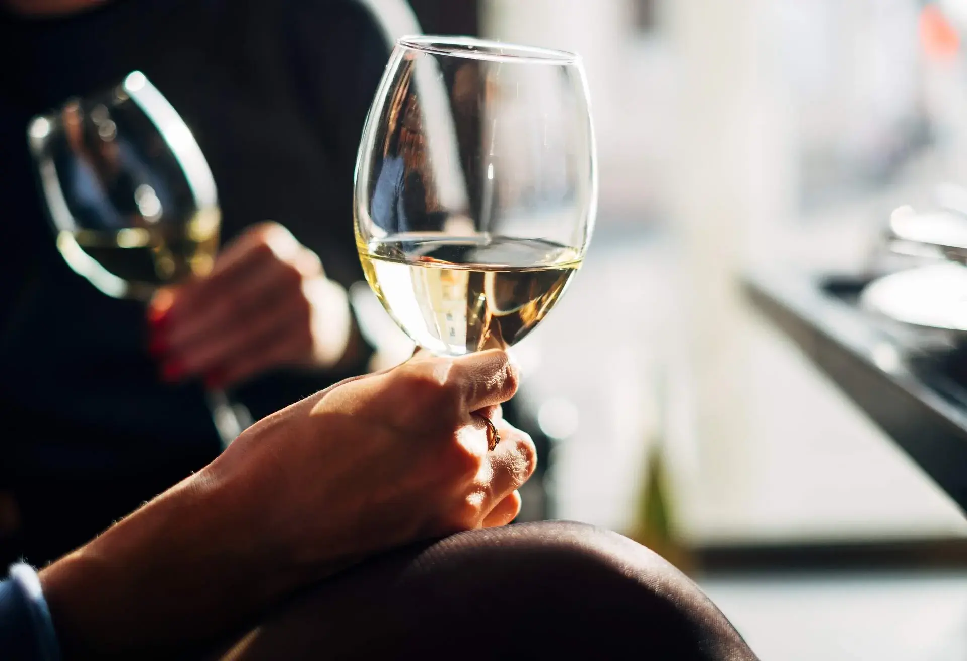 Two hands holding wine glasses filled with white wine.