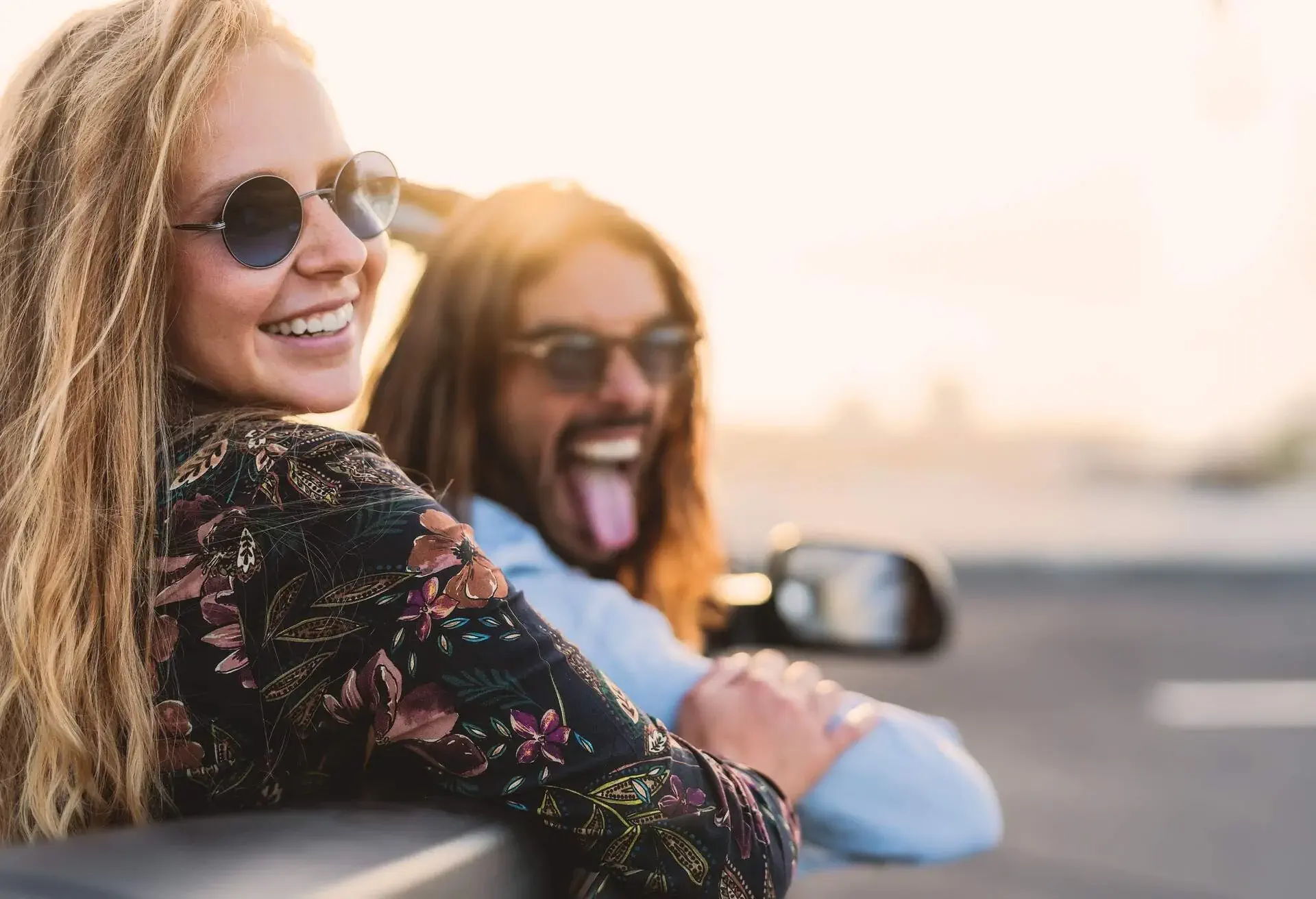 A happy couple in sunglasses smiles as they glances back while riding a car.