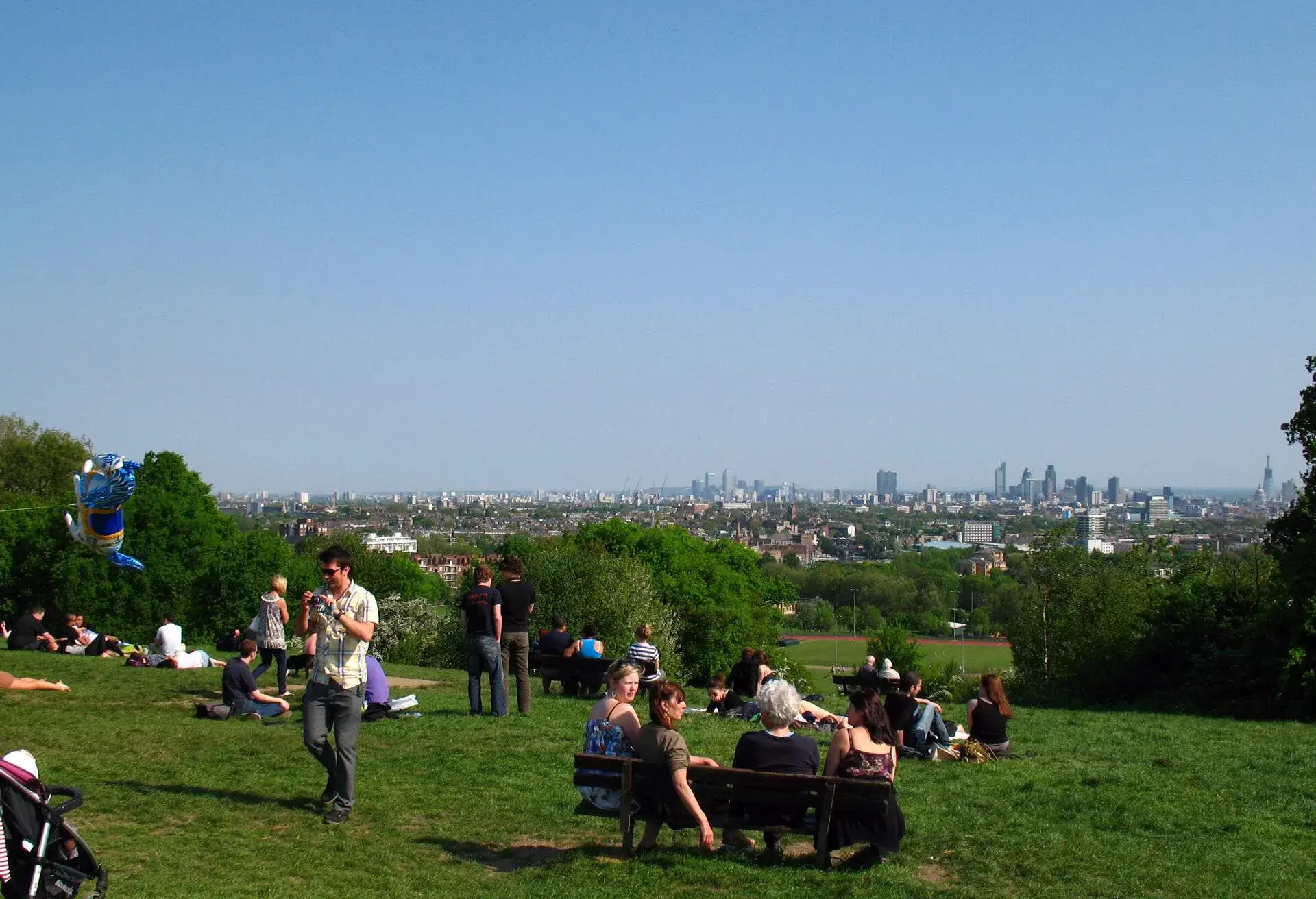 People enjoying a summer afternoon, and the view to the London City skyline, on Parliament Hill in Hampstead Heath, a large park in Hampstead, London, England, United Kingdom.