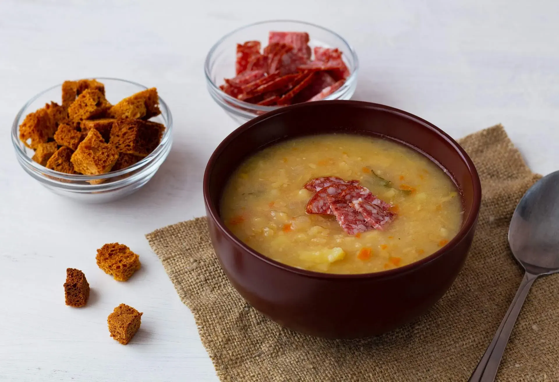 pea soup.The brown bowl of vegetable soup with meat and crackers. Pea soup with ham and potatoes with spoon on a white background. Classic Dutch pea soup erwtensoep, snert with bacon on the table.