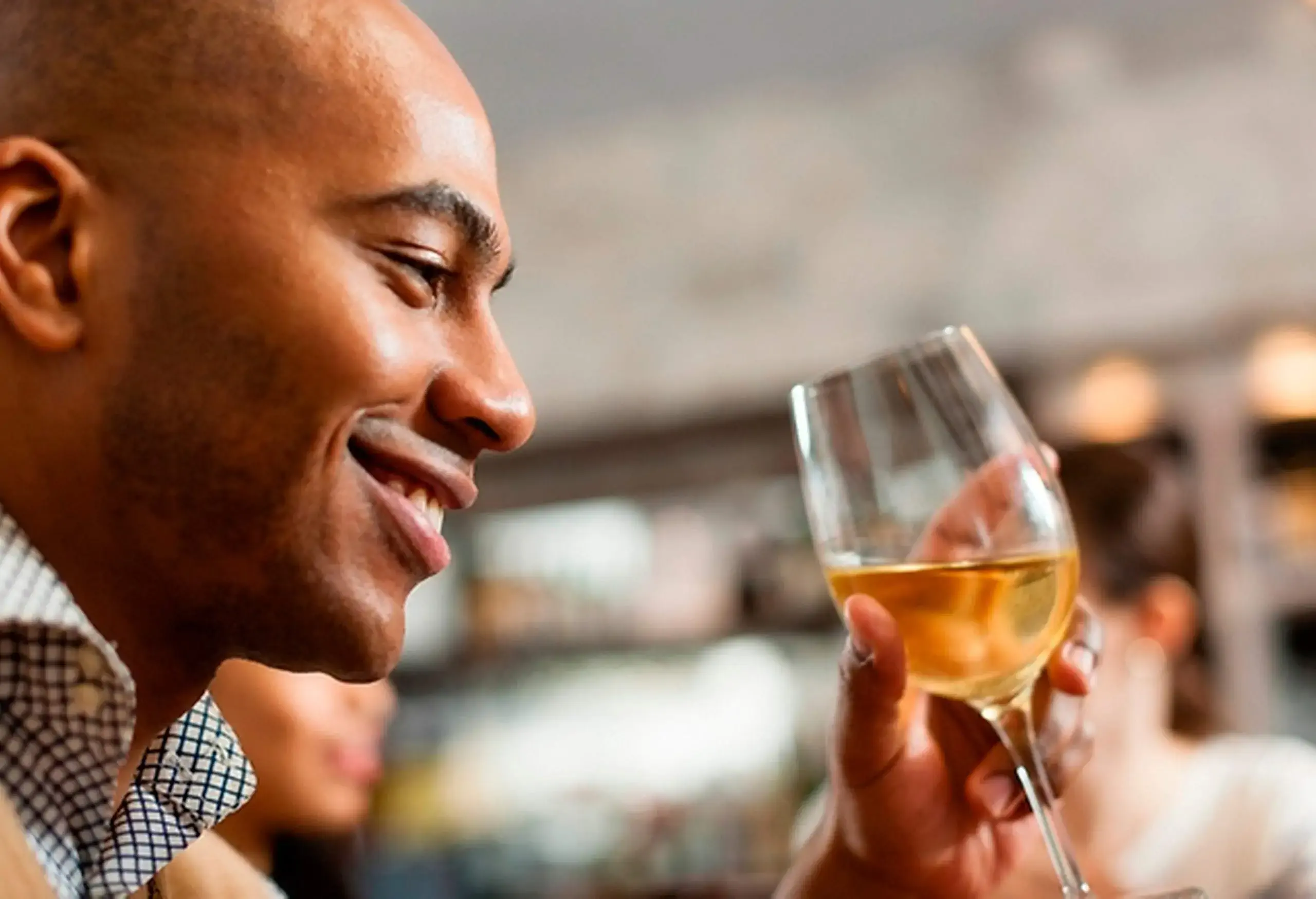 A smiling man holds a glass of white wine.