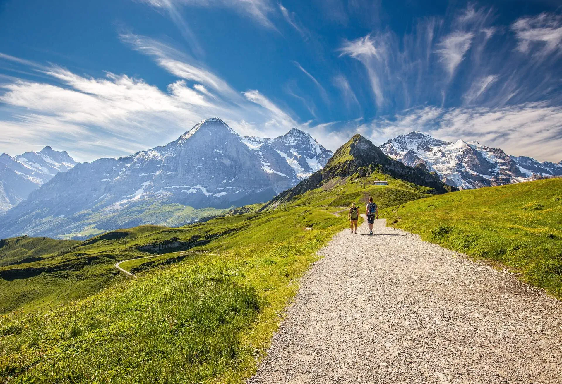 Young couple hiking in panorama trail leading to Kleine Scheidegg from Mannlichen with Eiger, Monch and Jungfrau mountain (Swiss Alps) in the background, Berner Oberland, Grindelwald, Switzerland