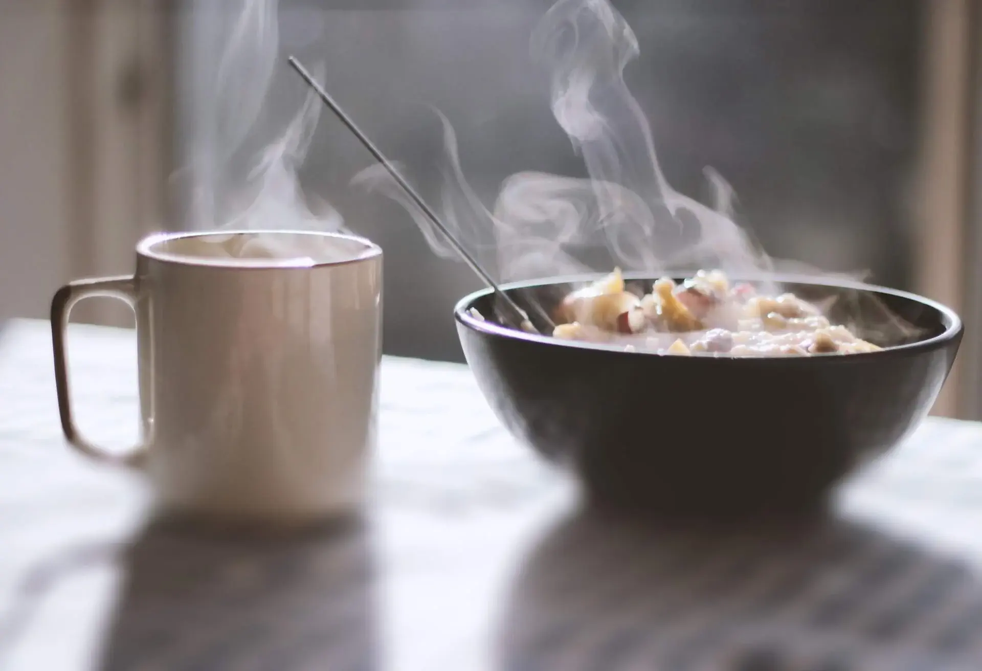 Close-up of porridge and tea served in a bowl on table with morning light and shadows coming through the window in the background.