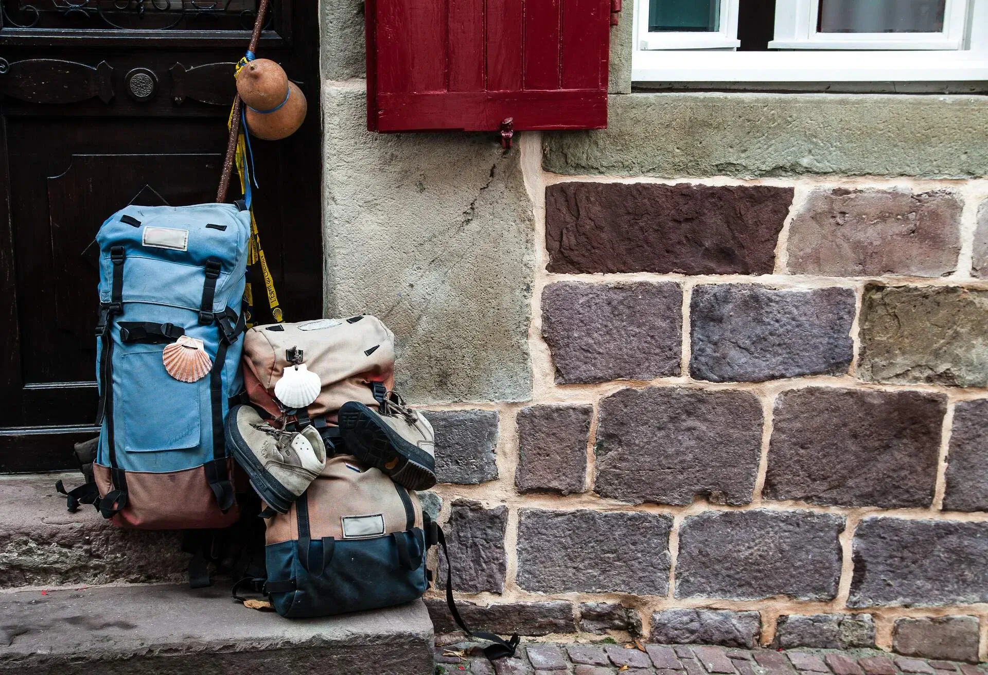 Two backpacks stood on the steps in front of the door of a building with red windows and brick walls.