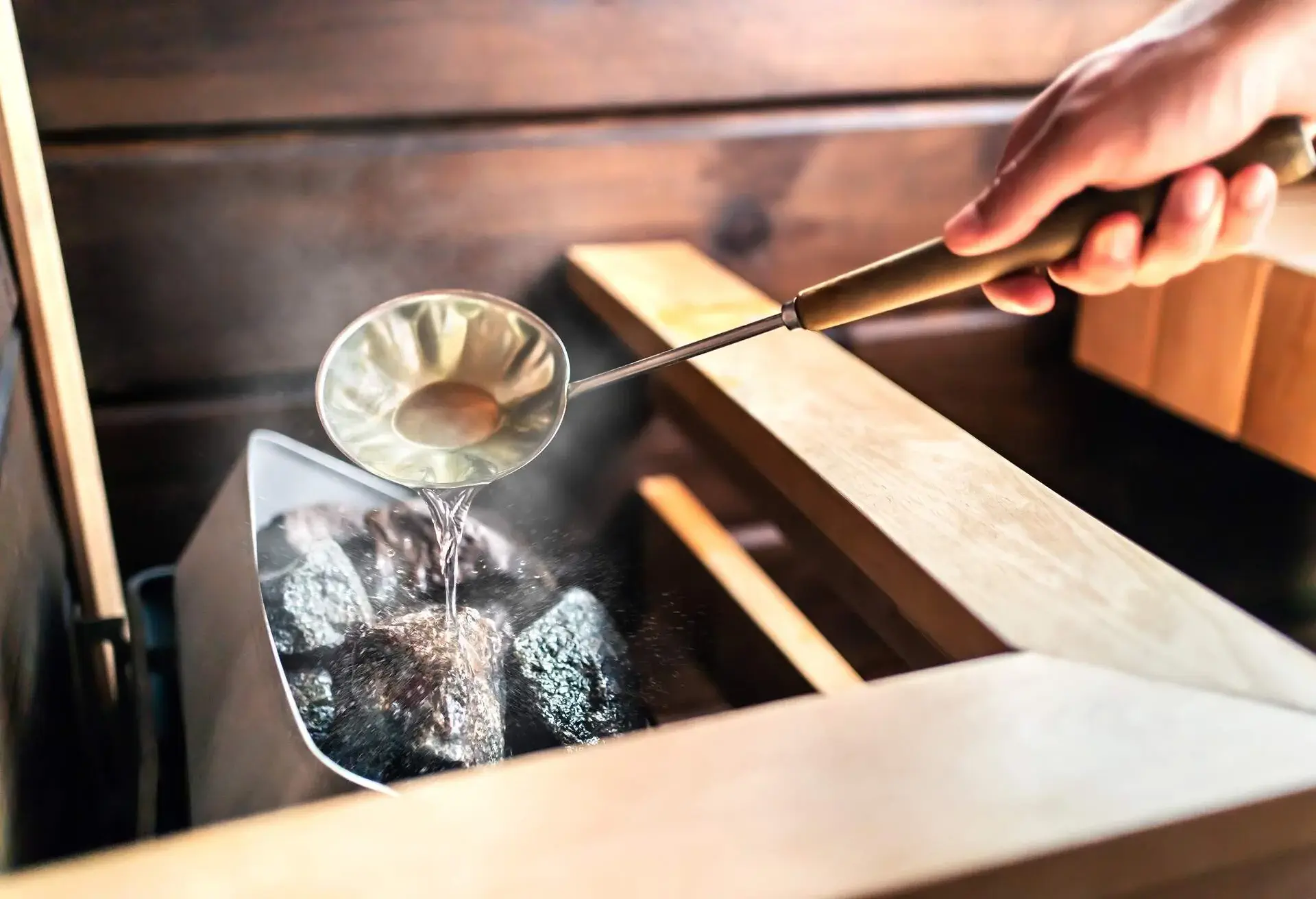 THEME_SPA_WELLNESS_HEALTH_ROOM_HOT_STEAM_WATER_STONES_MAN_HAND_GettyImages-1400278643