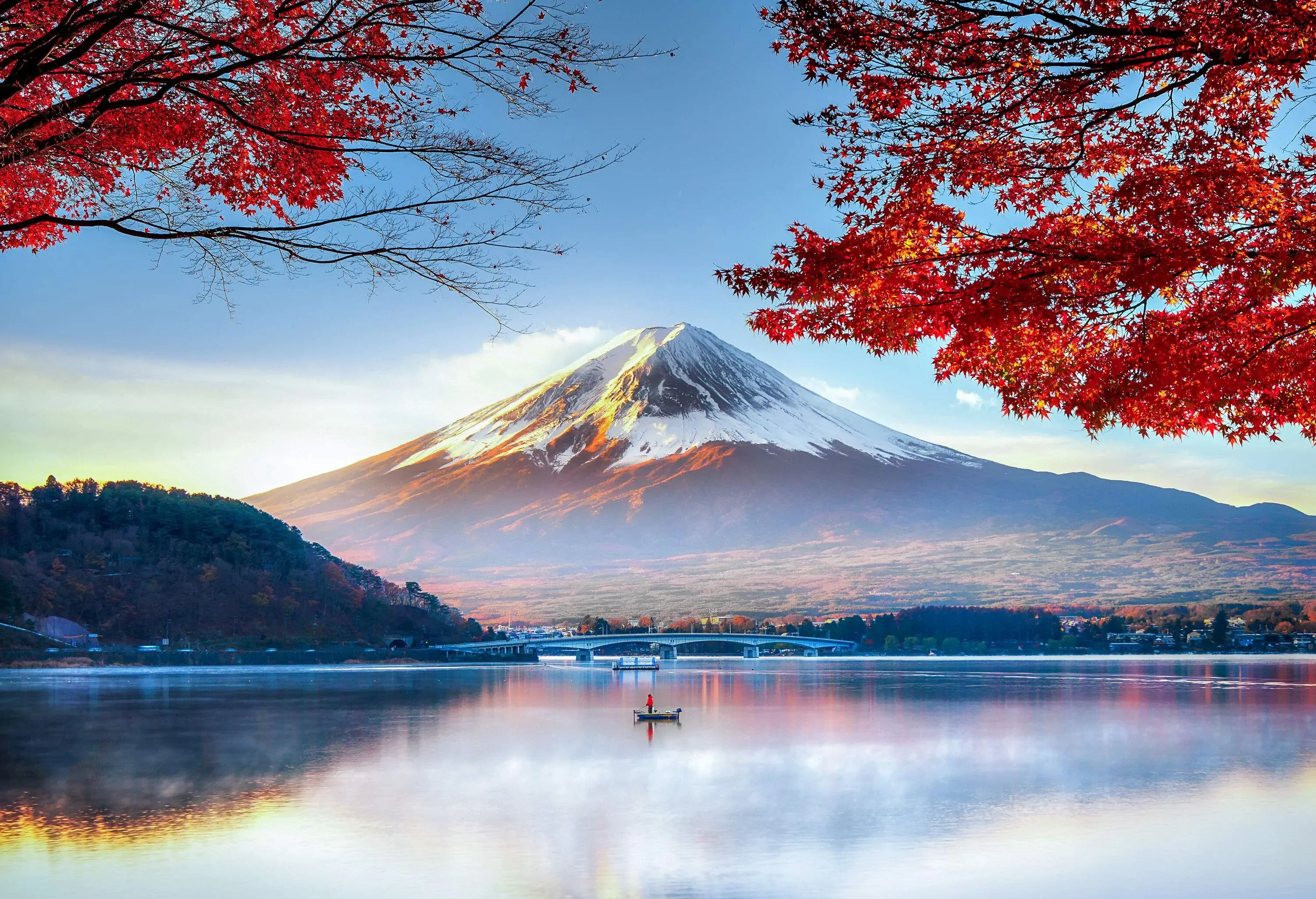 An individual on a scenic lake reflecting autumn's vibrant colours with a view of the awe-inspiring beauty of the snow-capped Mount Fuji in Japan.