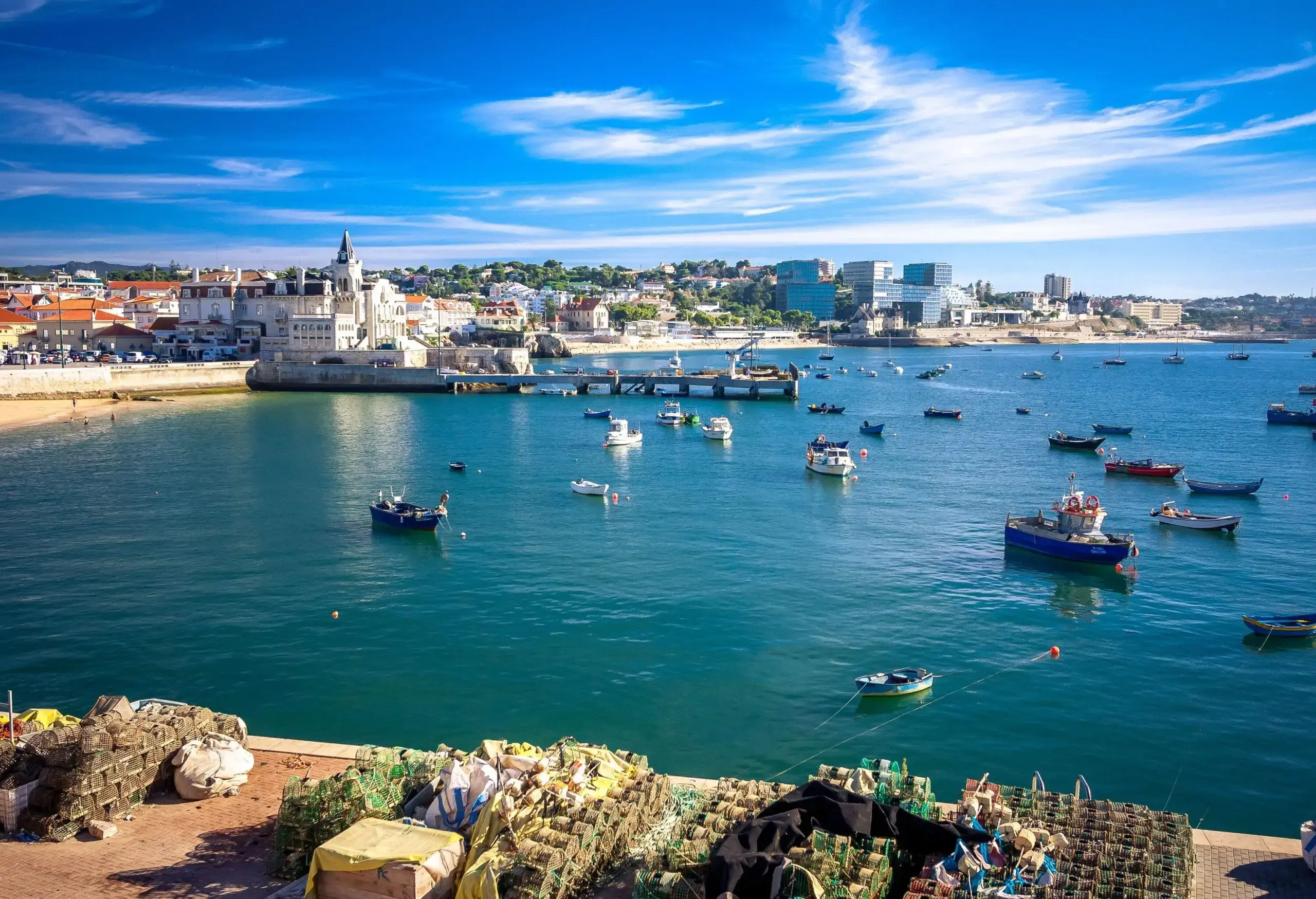 A port with stacks of lobster traps overlooking a cityscape and a harbour full of anchored boats.