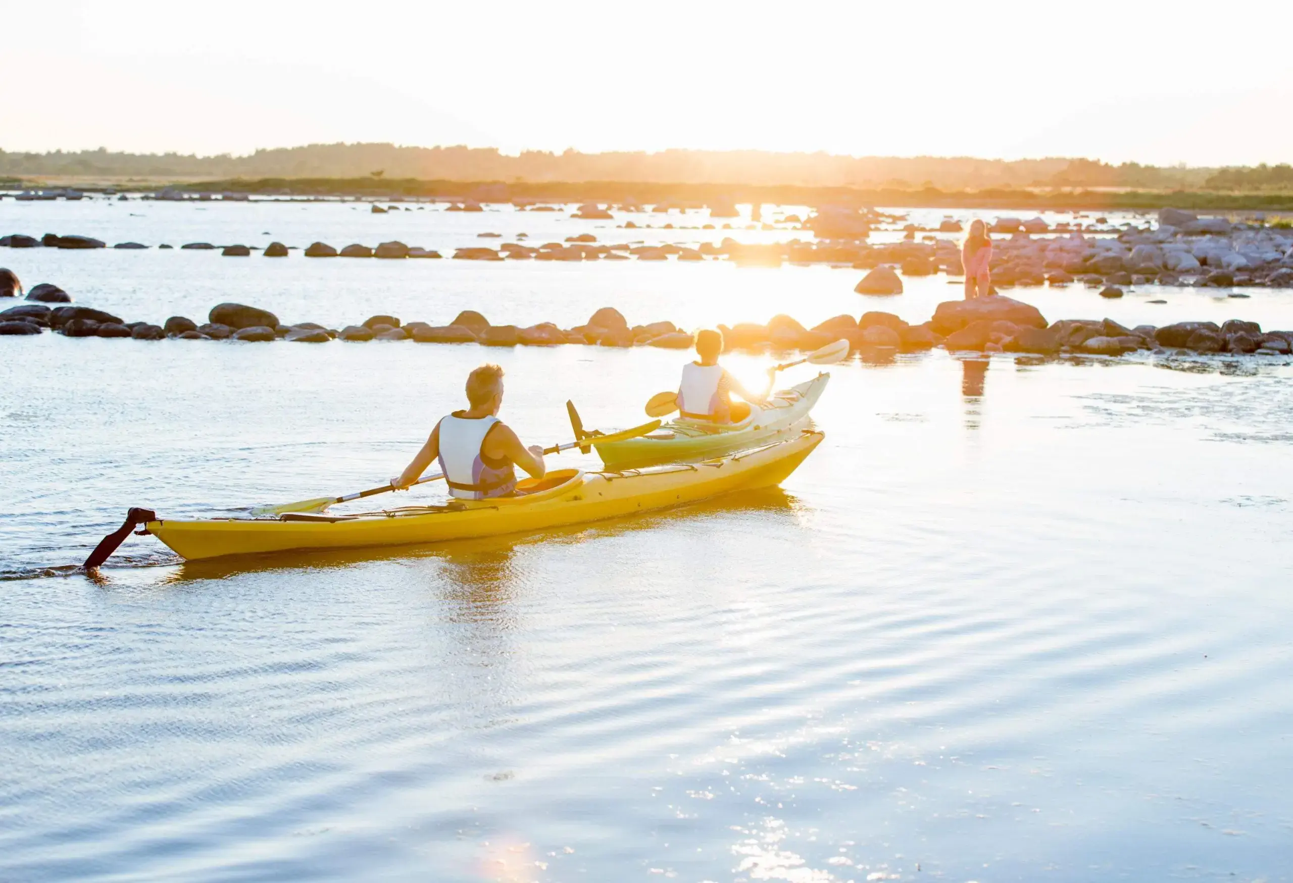 Two people kayaking in the sea close to the shore as the evening light shines on.