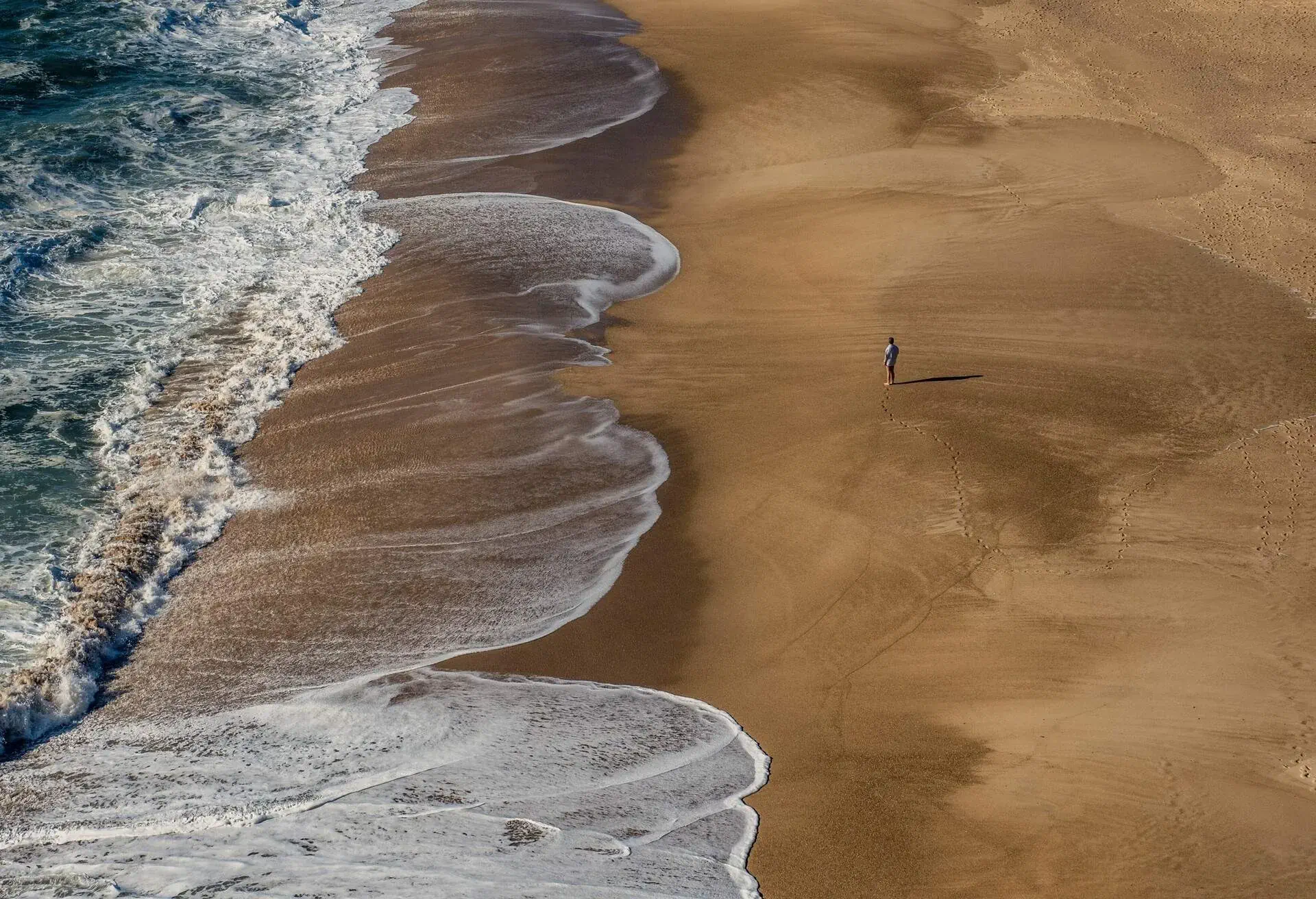 Man standing on empty beach in Nazaré, Portugal
