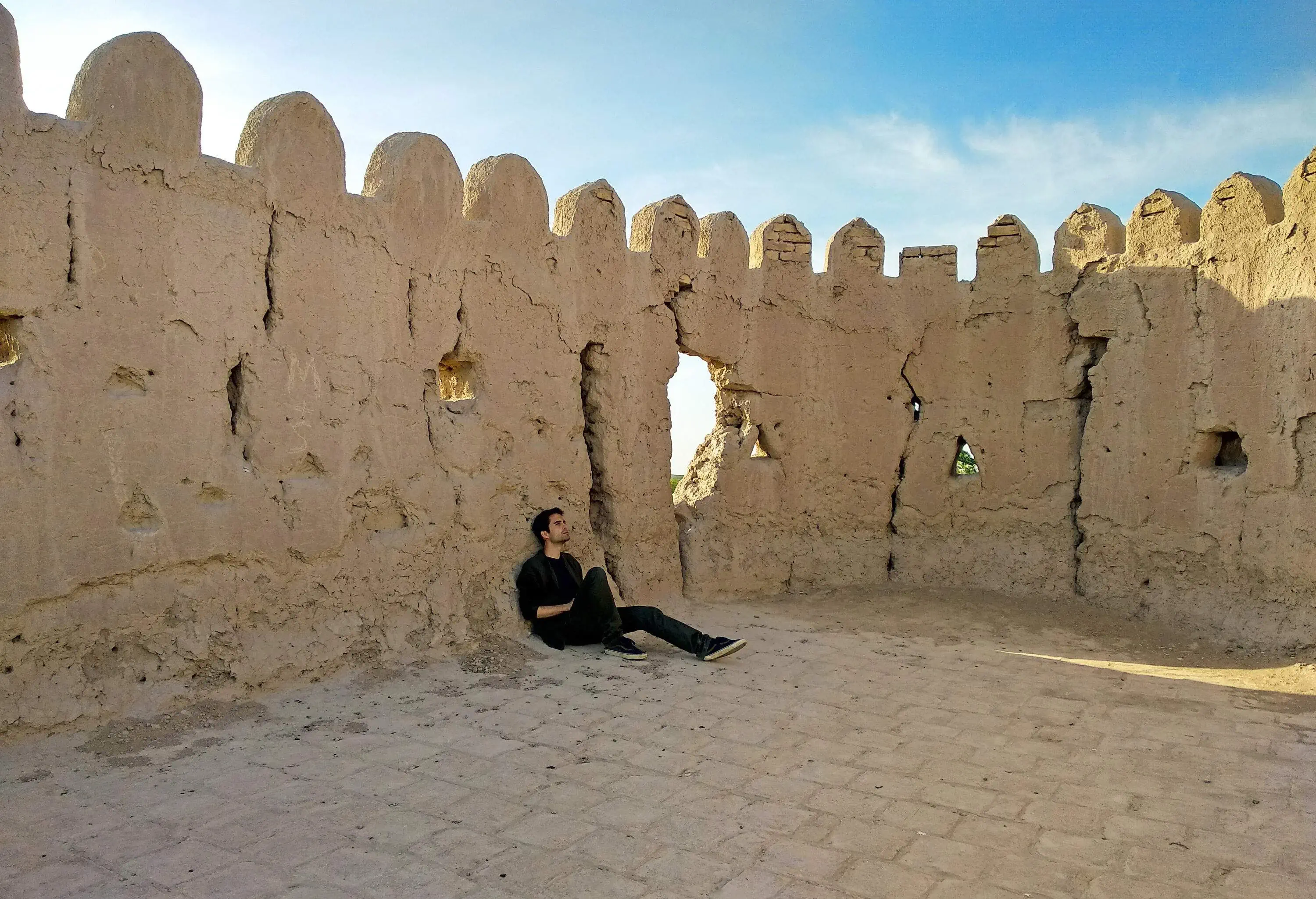 A person finds solace by resting and leaning against a weathered and cracked wall.