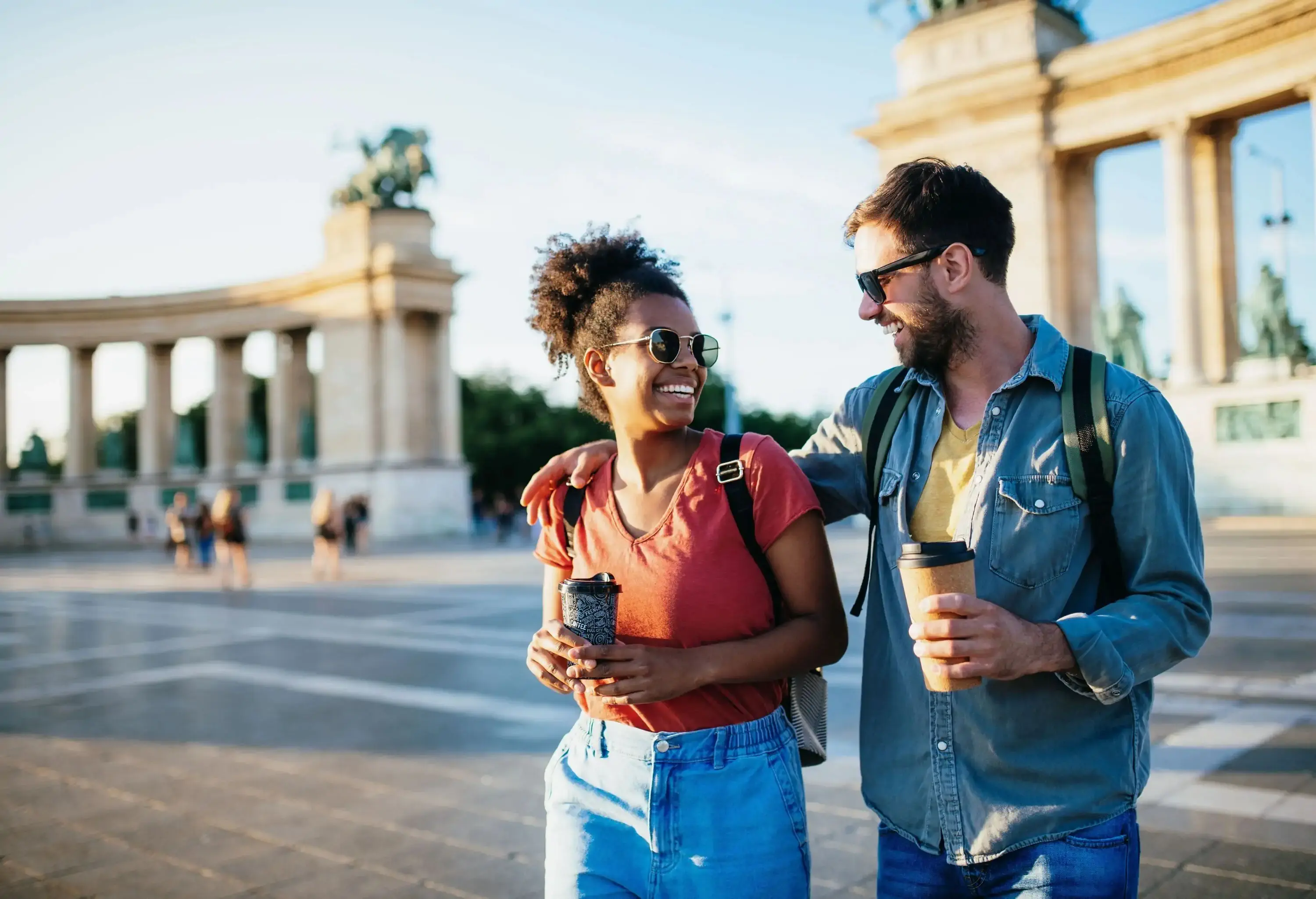 Couple laughing and walking with a to go coffee near a monument