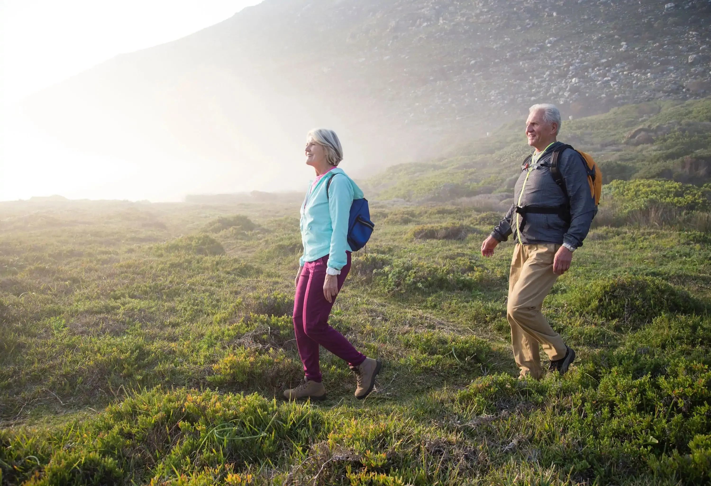 A senior couple walking through the rugged meadow on a foggy mountainside.
