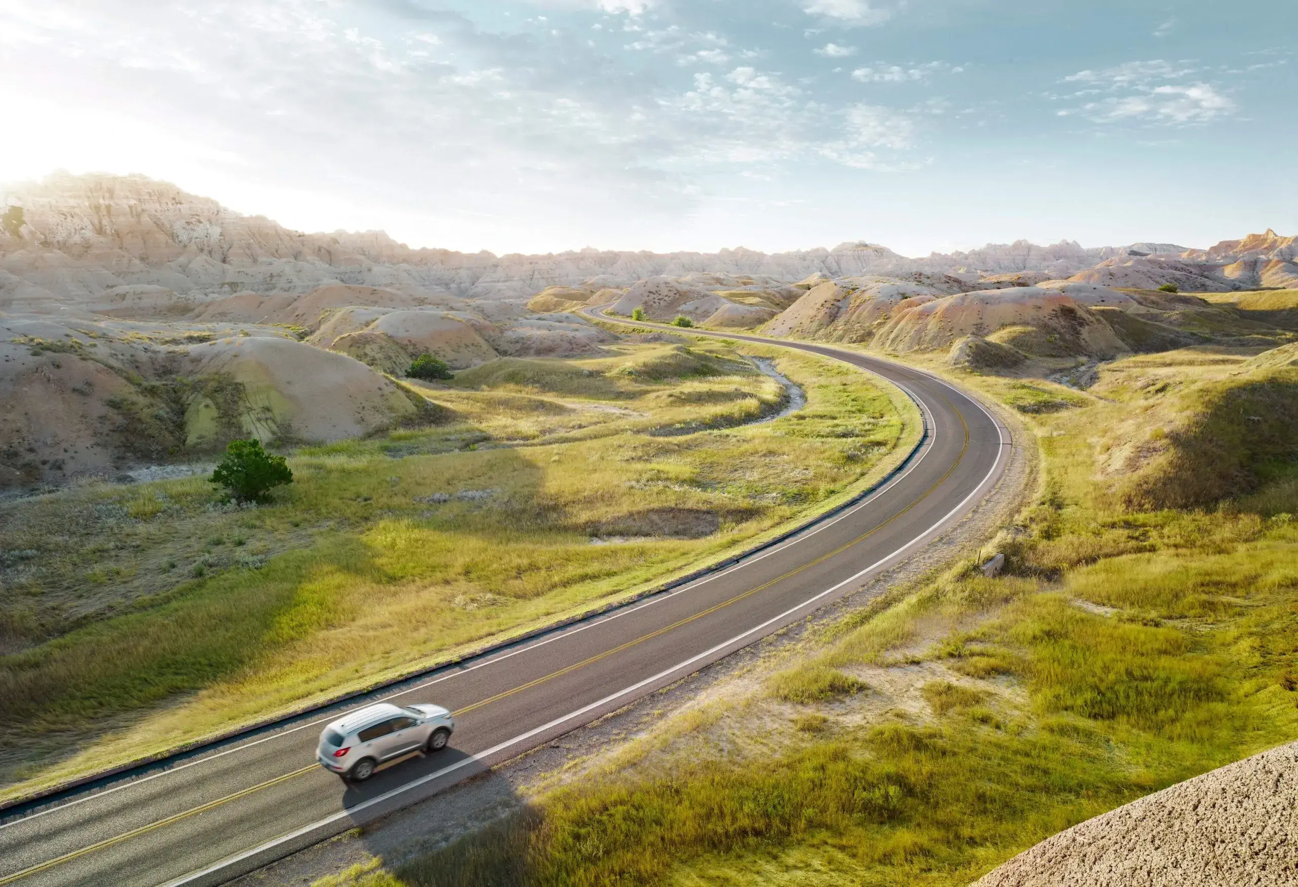 A silver car travels on a road across a hilly landscape.