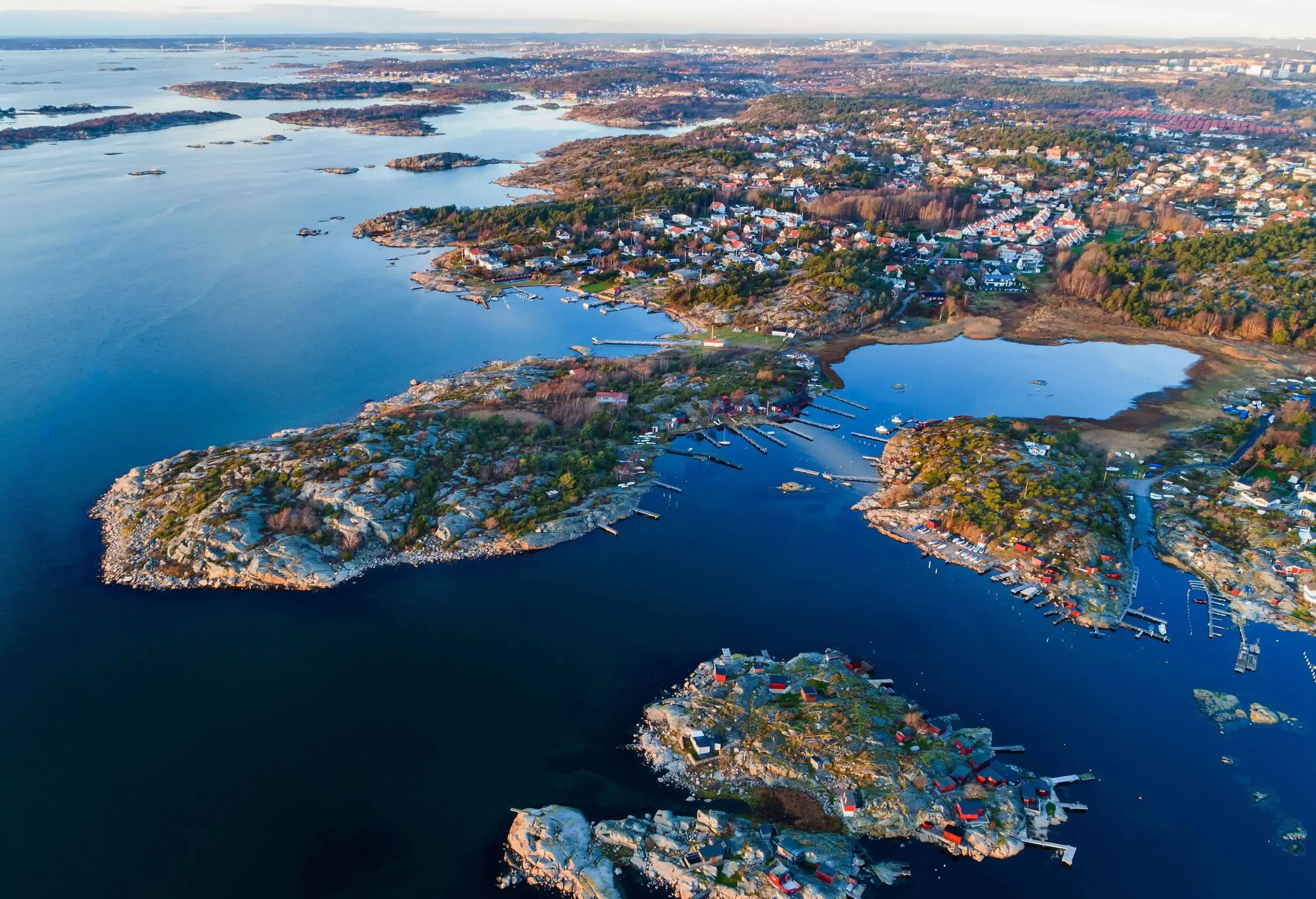 An aerial view of a sea containing small scattered islands easily reachable from a coastal town packed with houses.