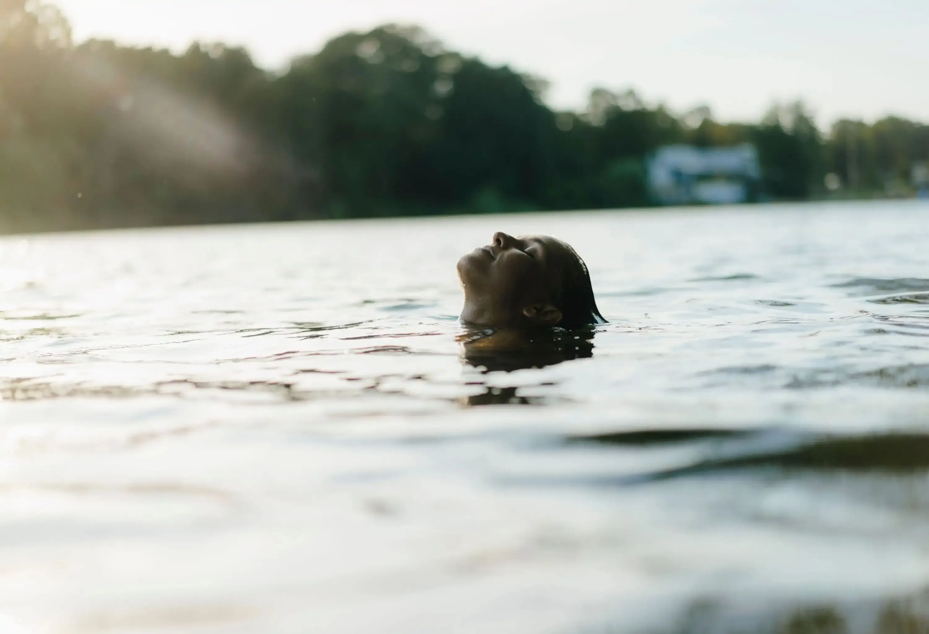 A head of a person with closed eyes emerges from the lake's surface.