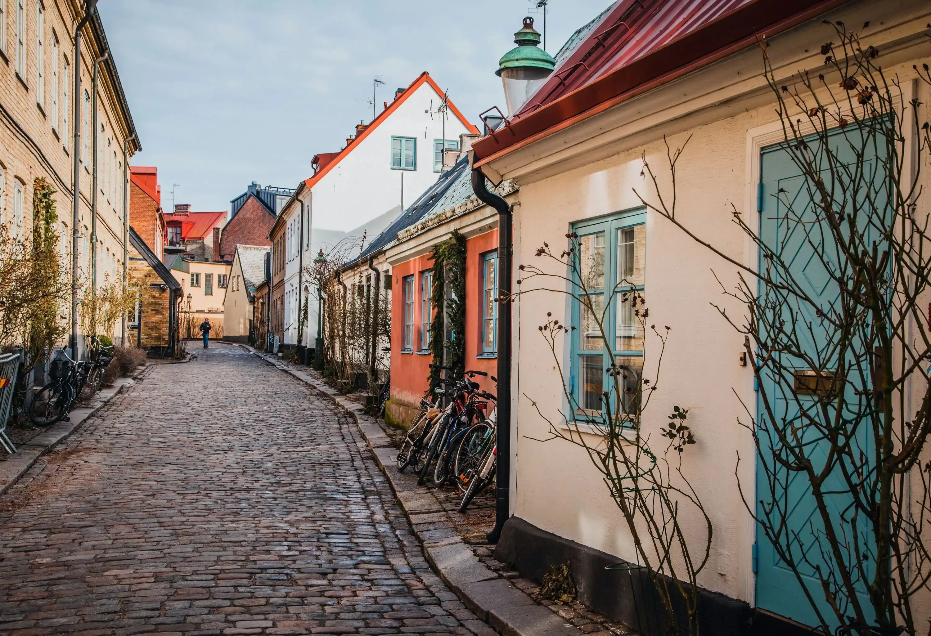 A man in the distance entering a paved alley with bicycles parked outside the houses.
