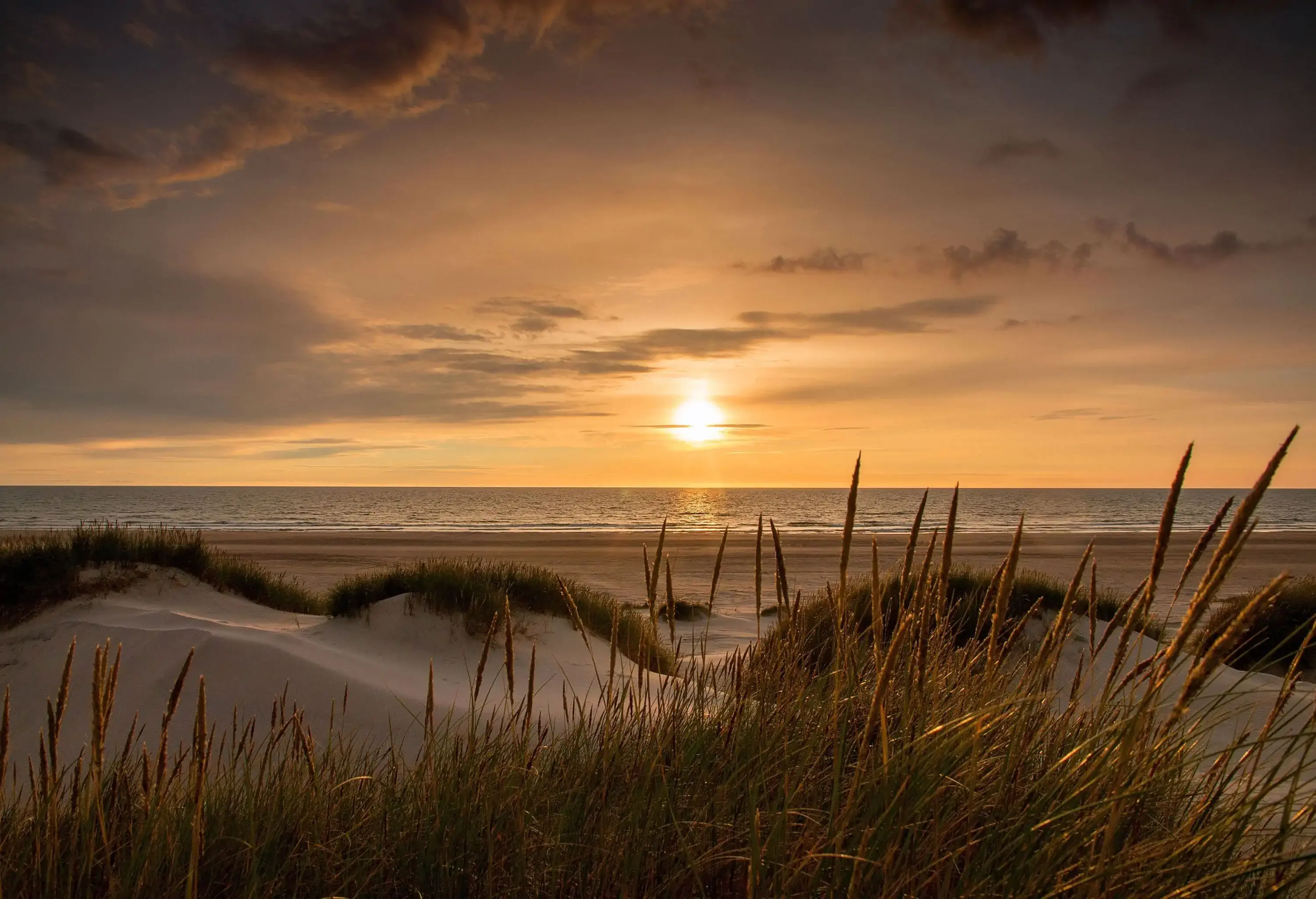 A romantic atmosphere on the beach with the sun glowing amid the murky skies over the sea.