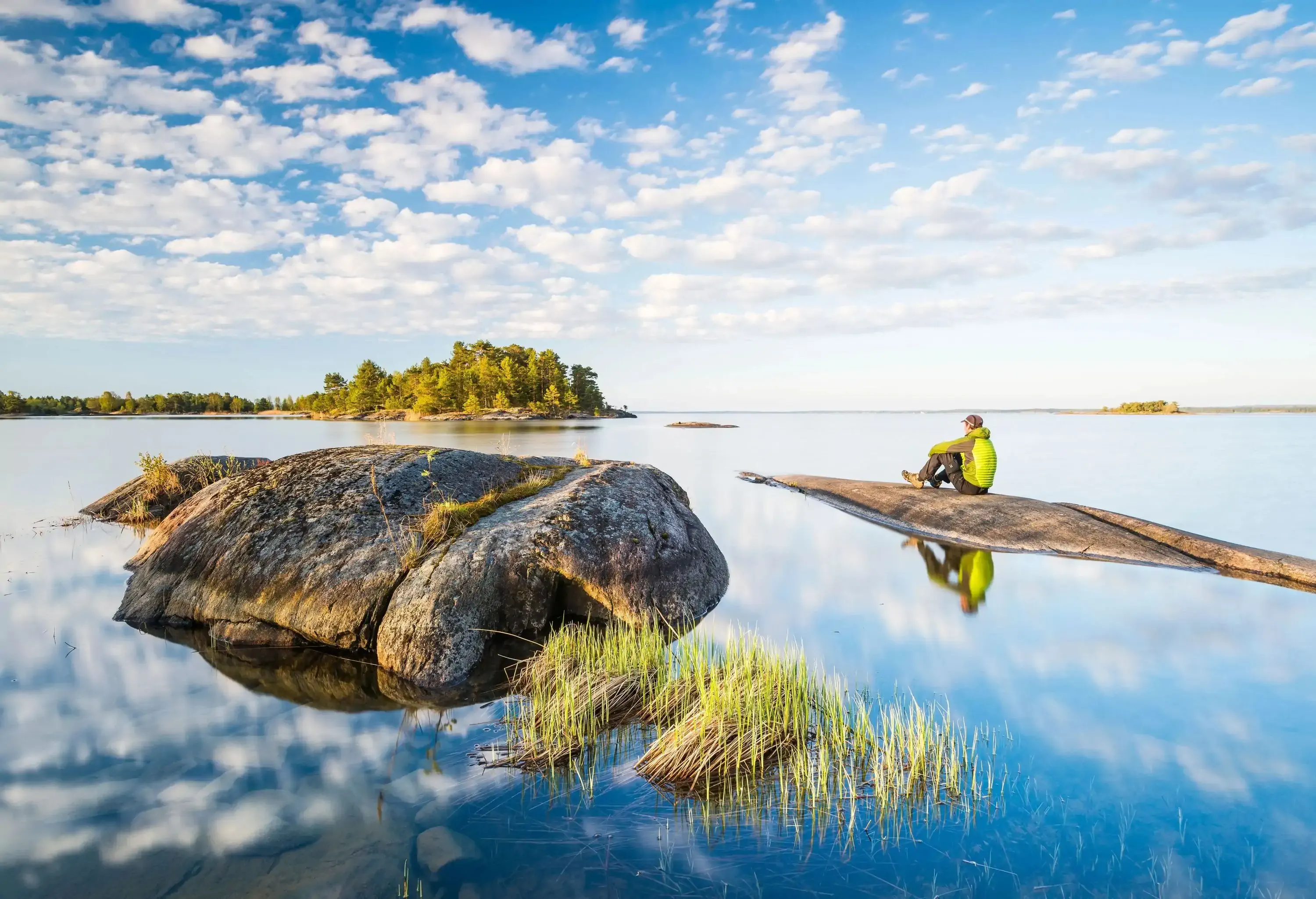 A man sitting on a sunken rock in a lake gazing out at the nature around him.