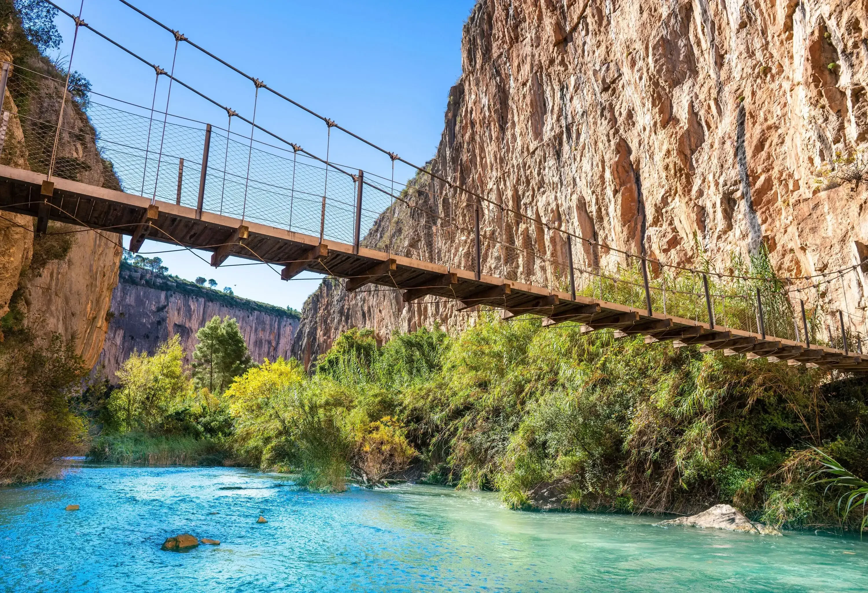 A suspension bridge between mountain cliffs over a river of turquoise water.