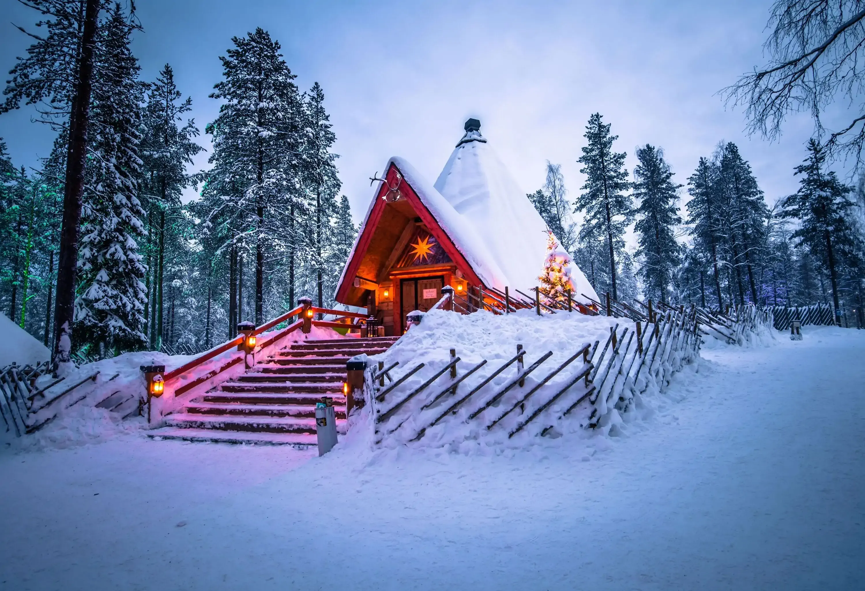 A cabin in the woods with the rooftops blanketed in a thick layer of snow.
