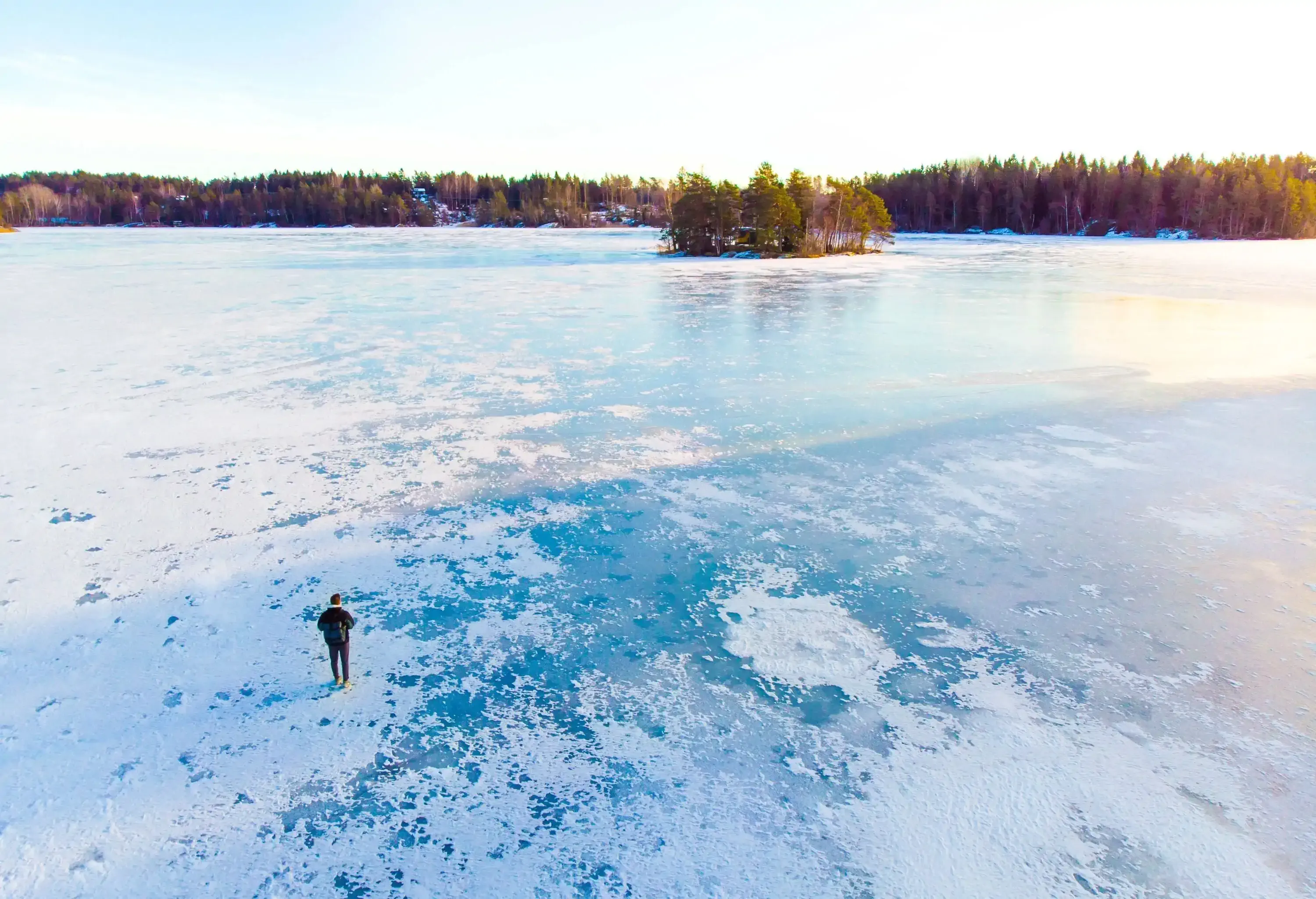 A person on a frozen lake gazing out on a forested island and its surroundings.