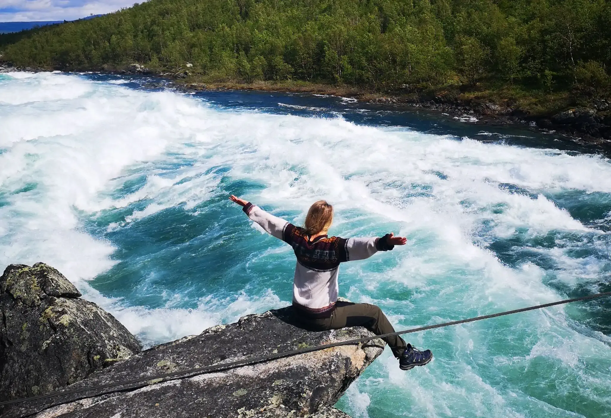 A woman perched on a hanging cliff with outstretched arms over a raging sea.