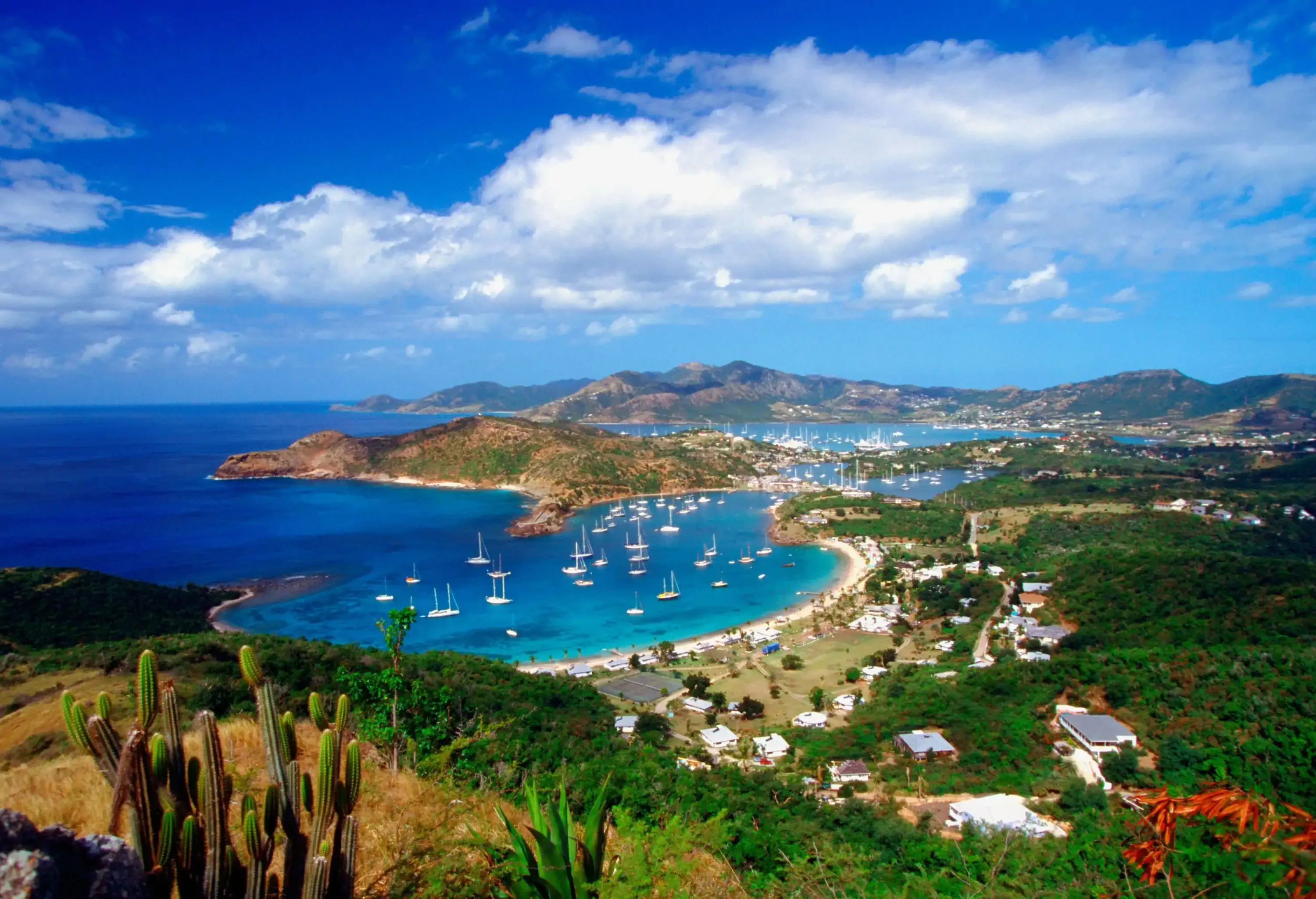 A crescent beach on a turquoise horseshoe-shaped bay with docked boats against the dramatic sky.