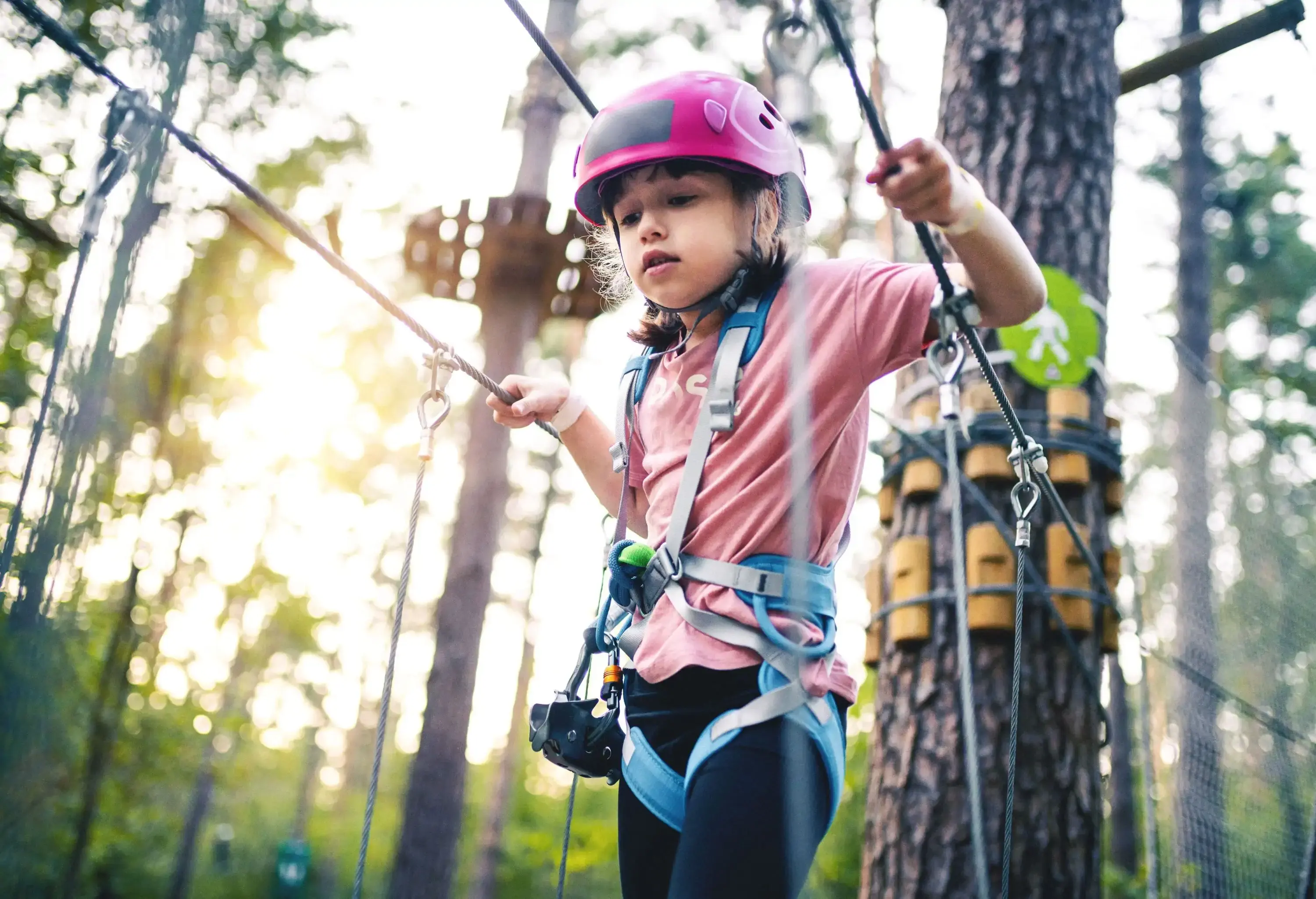 A spirited girl navigates an adventure park with confidence, donning safety gear and gripping ropes as she traverses a challenging obstacle.