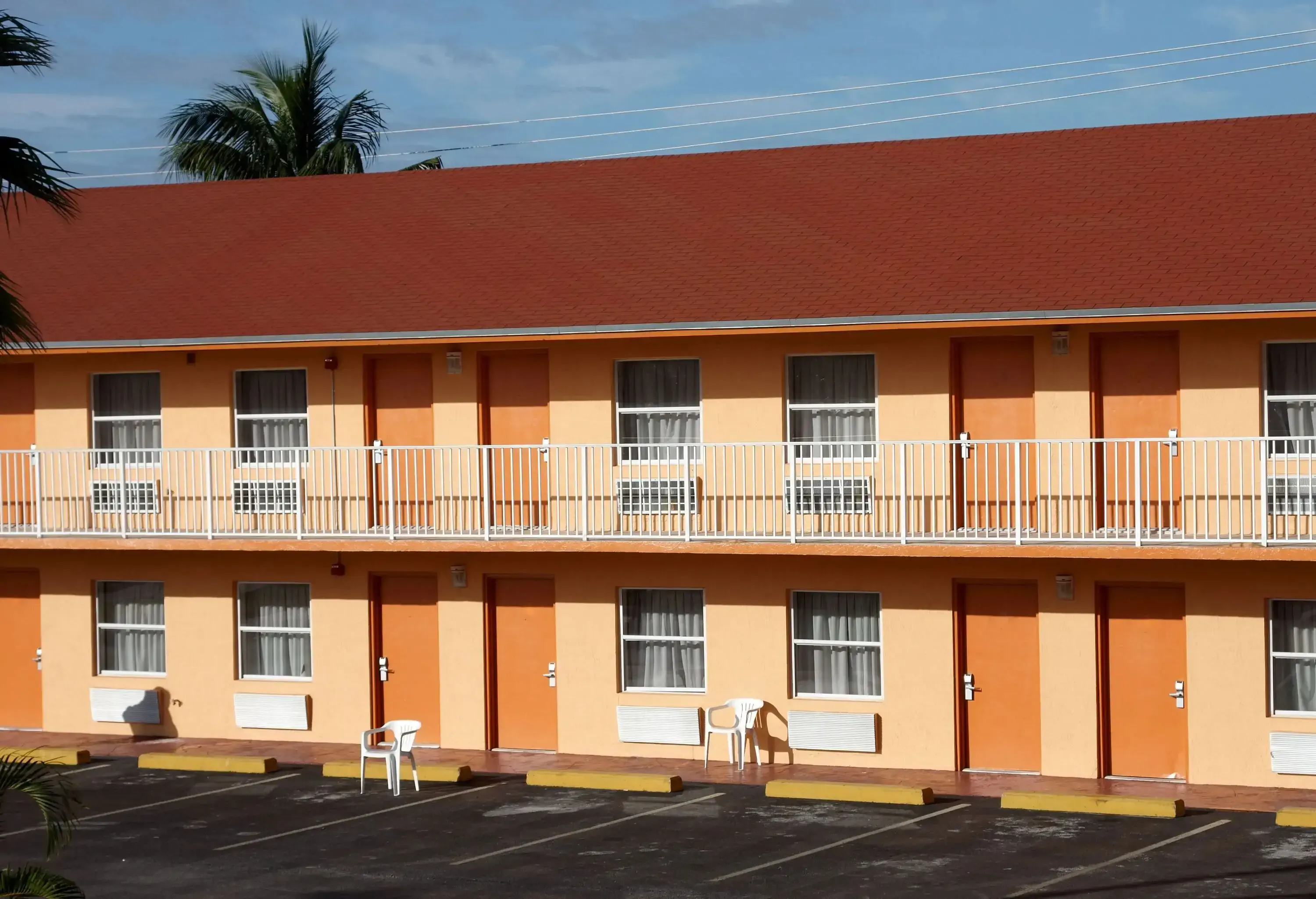 A two-level motel with multiple rooms and glass windows in front of a parking lot.
