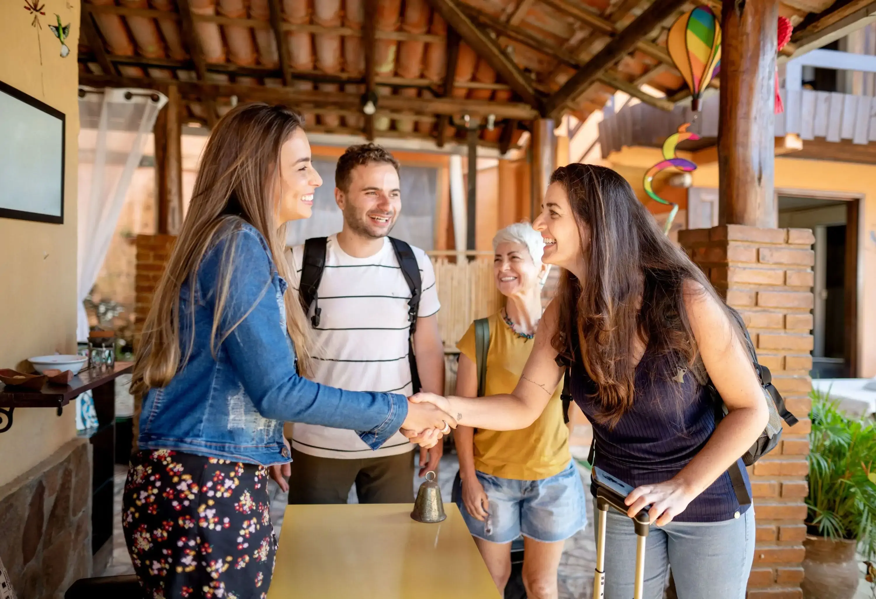 Smiling woman shaking hands and greeting a group of guests at a table outside of her holiday accommodation