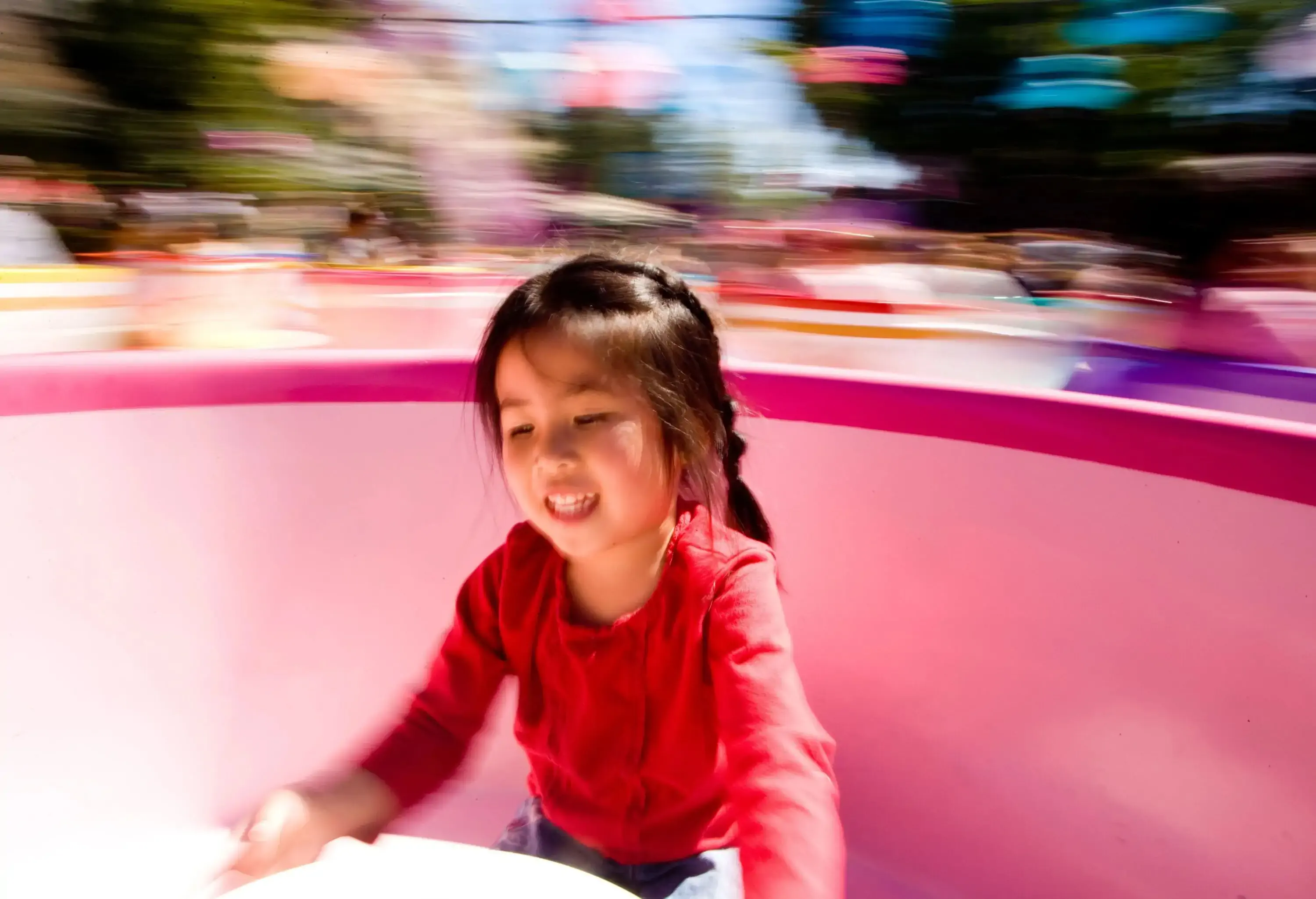 A gleeful girl in a vibrant red shirt whirls around on a colourful teacup ride.
