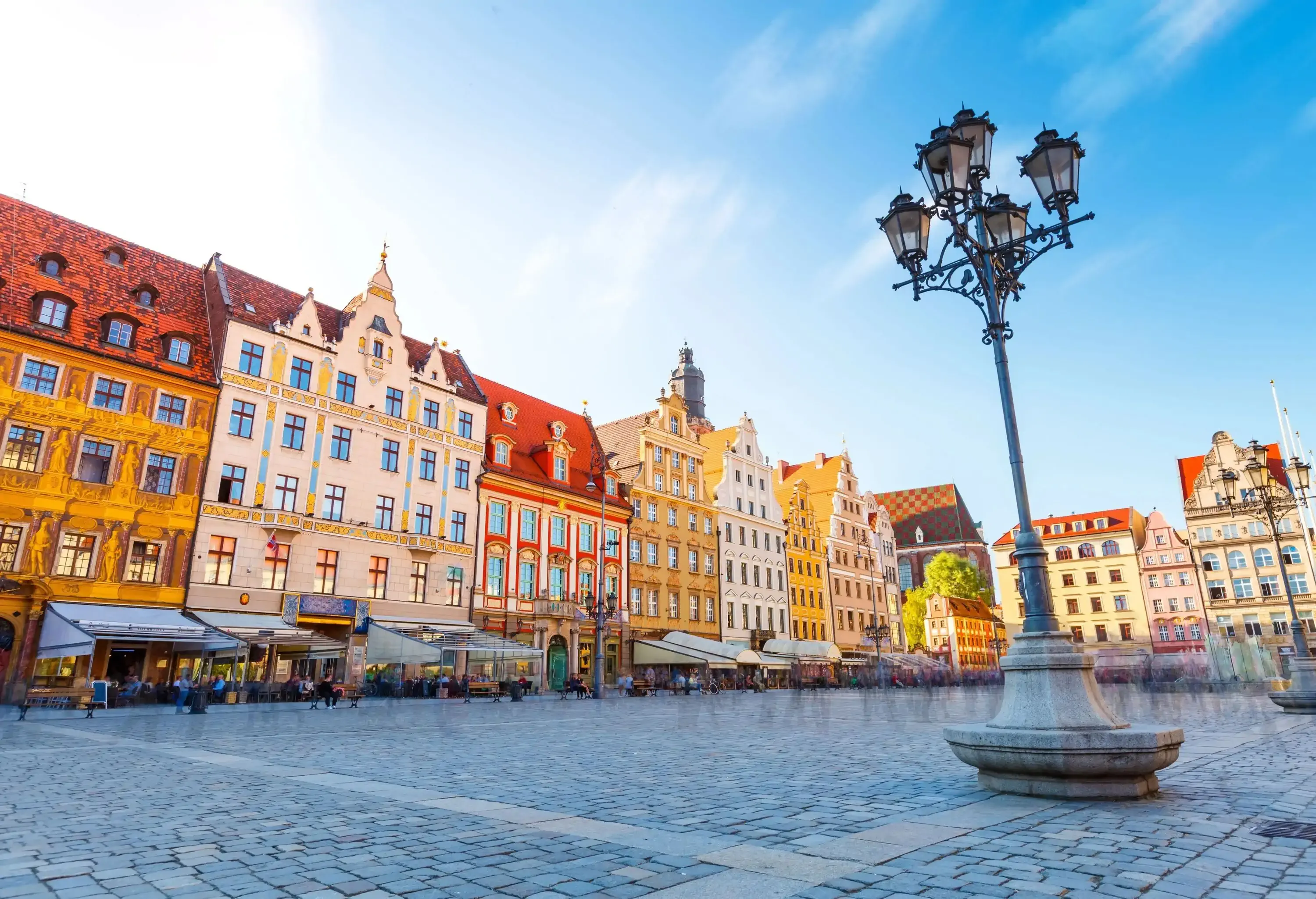 Colourful buildings and outdoor restaurants surrounding a town square with vintage street lamps.