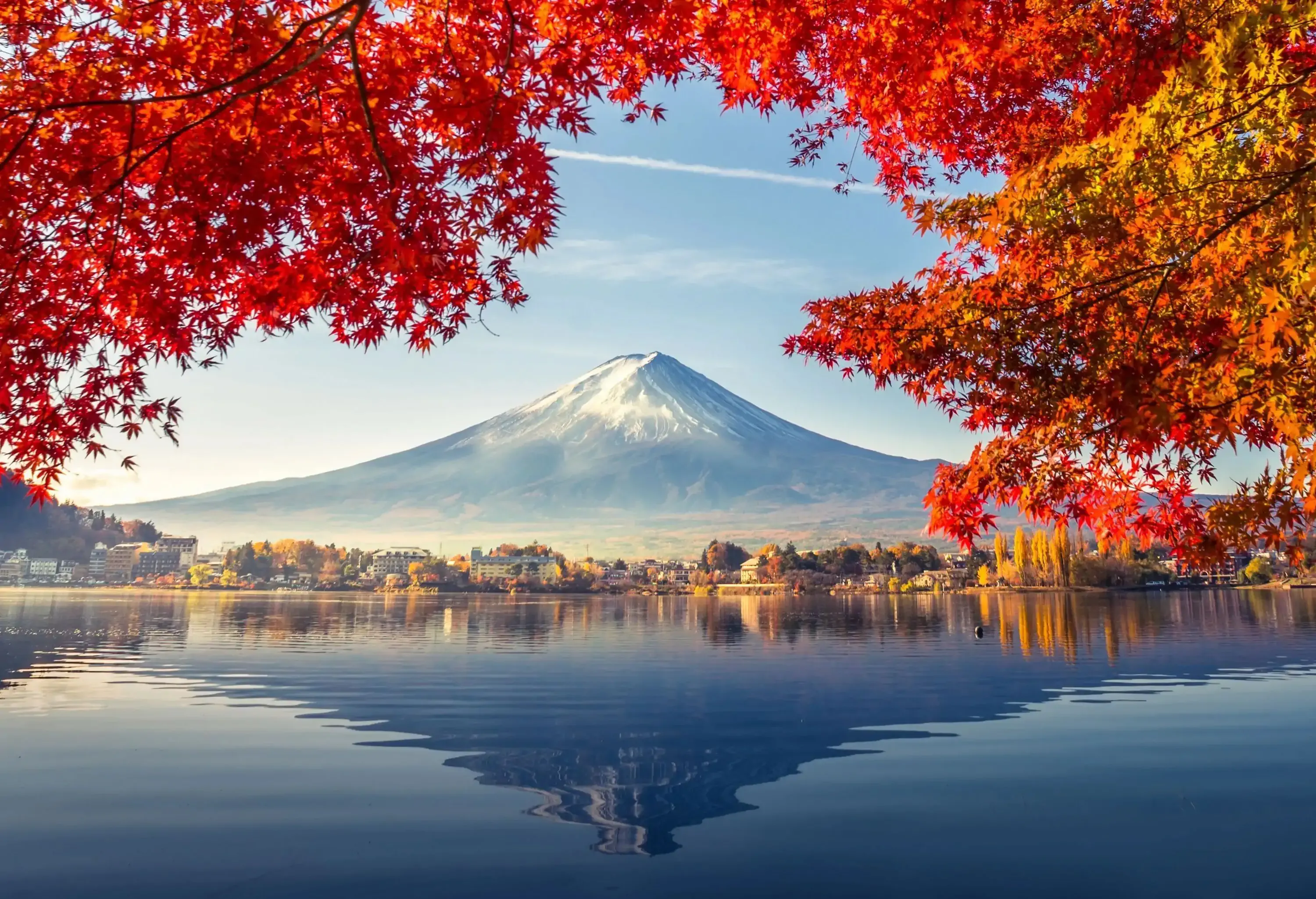 Mt. Fuji's majestic conical form framed by scarlet fall foliage and reflected on a clear lake.