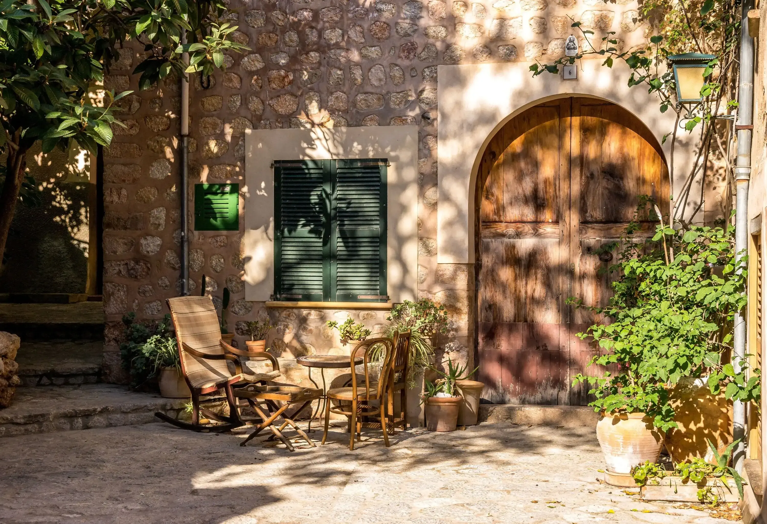 A small patio with table and chairs in front of a stone house with a large wooden arched door.