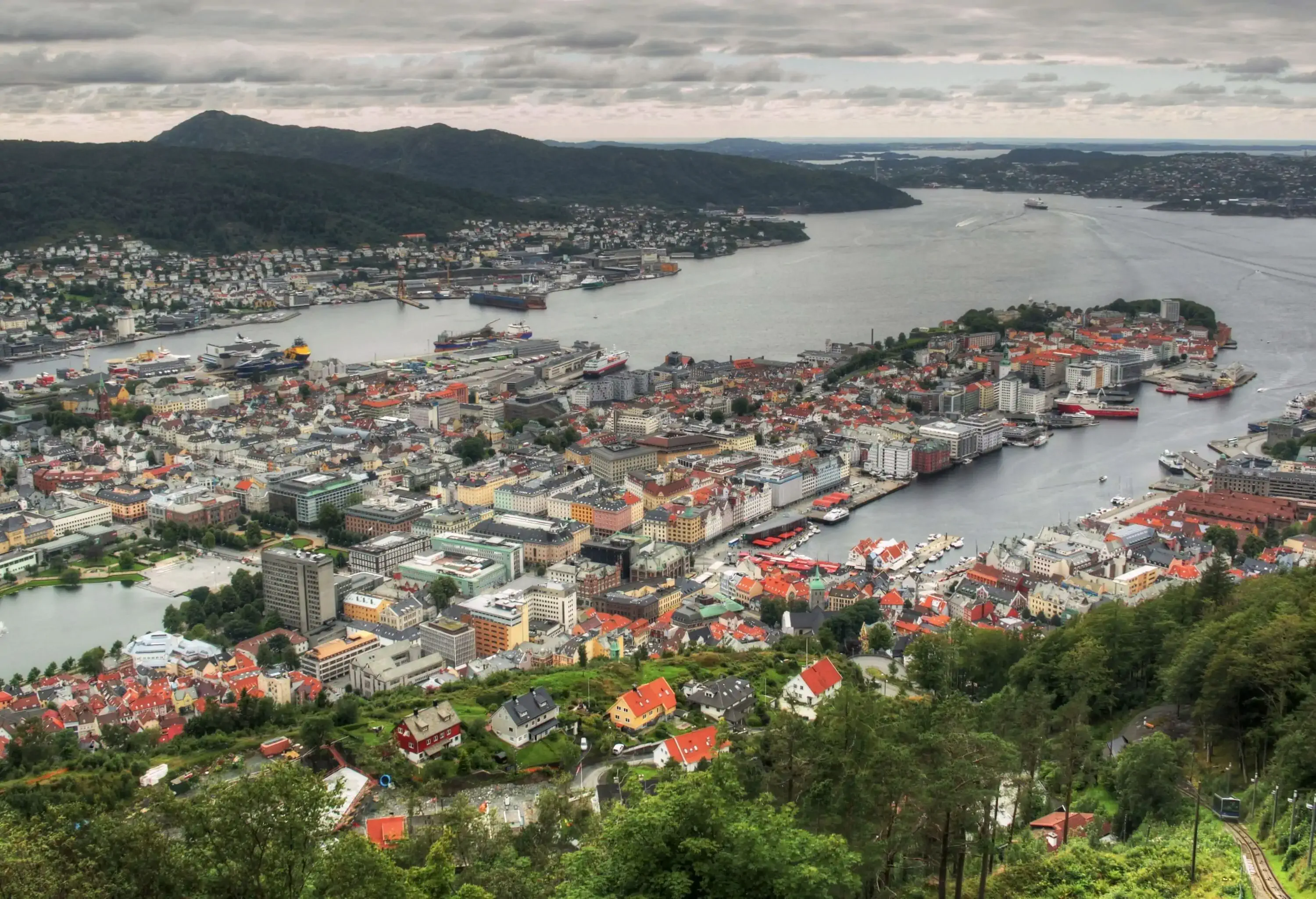 Aerial view of a seaside city beneath the lush mountain range against the cloudy sky.