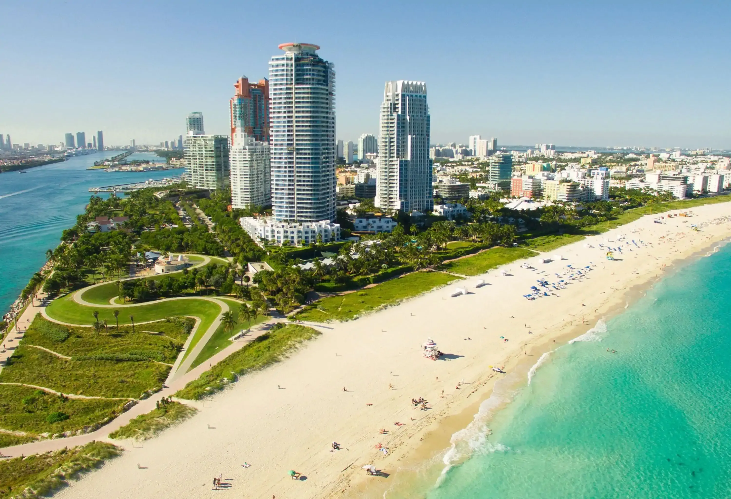 Aerial view of a coastal city with towering resort buildings and pristine white sand shore surrounded by the turquoise sea under the cloudy blue sky.