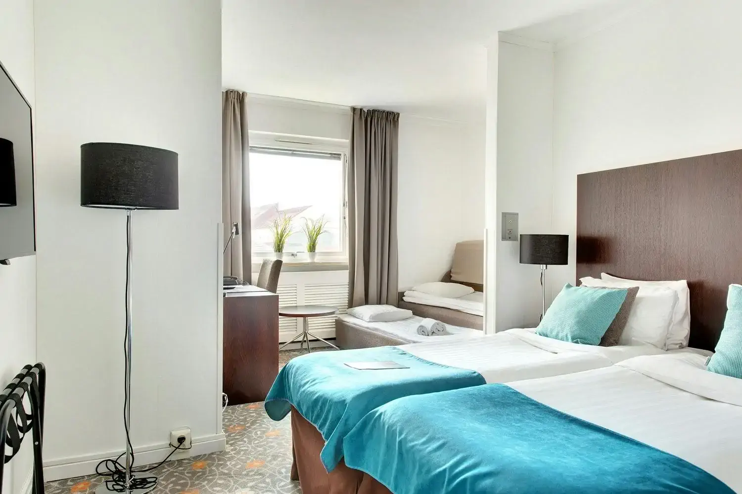 Contemporary hotel room with azure blankets and an extra bed