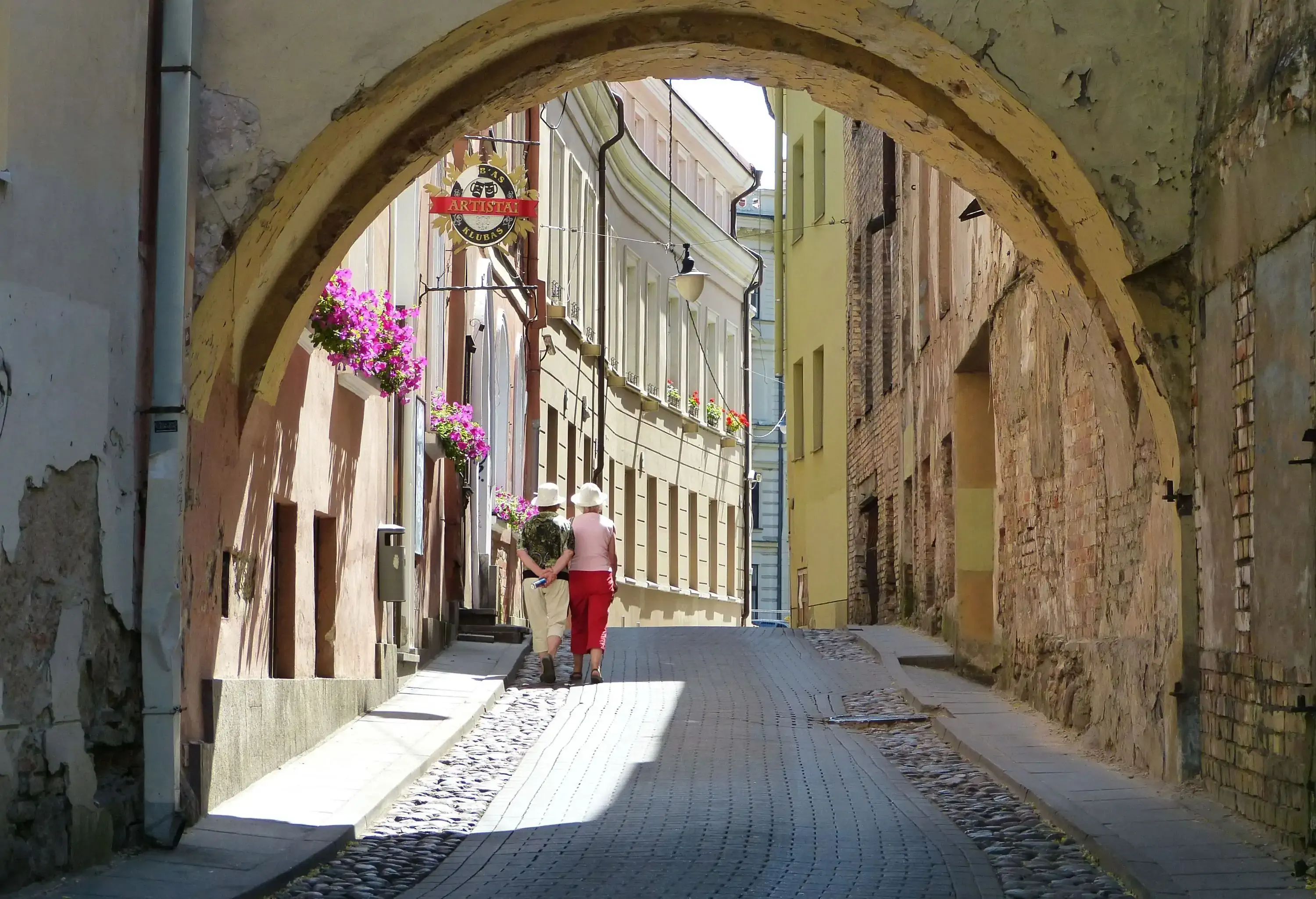 A deteriorating archway framing the two women walking along a steep cobbled path.