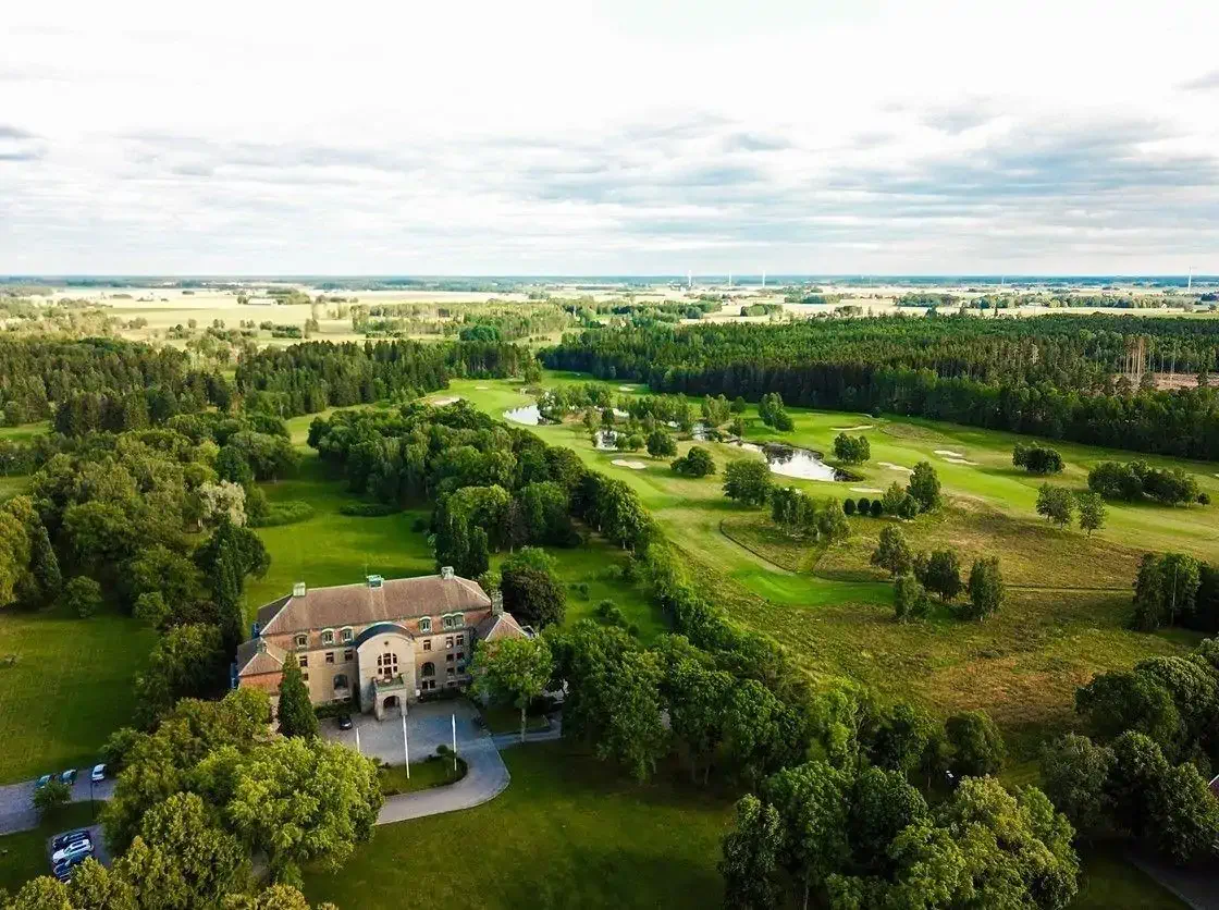 Aerial view of a castle surrounded by green fields and trees on a cloudy day