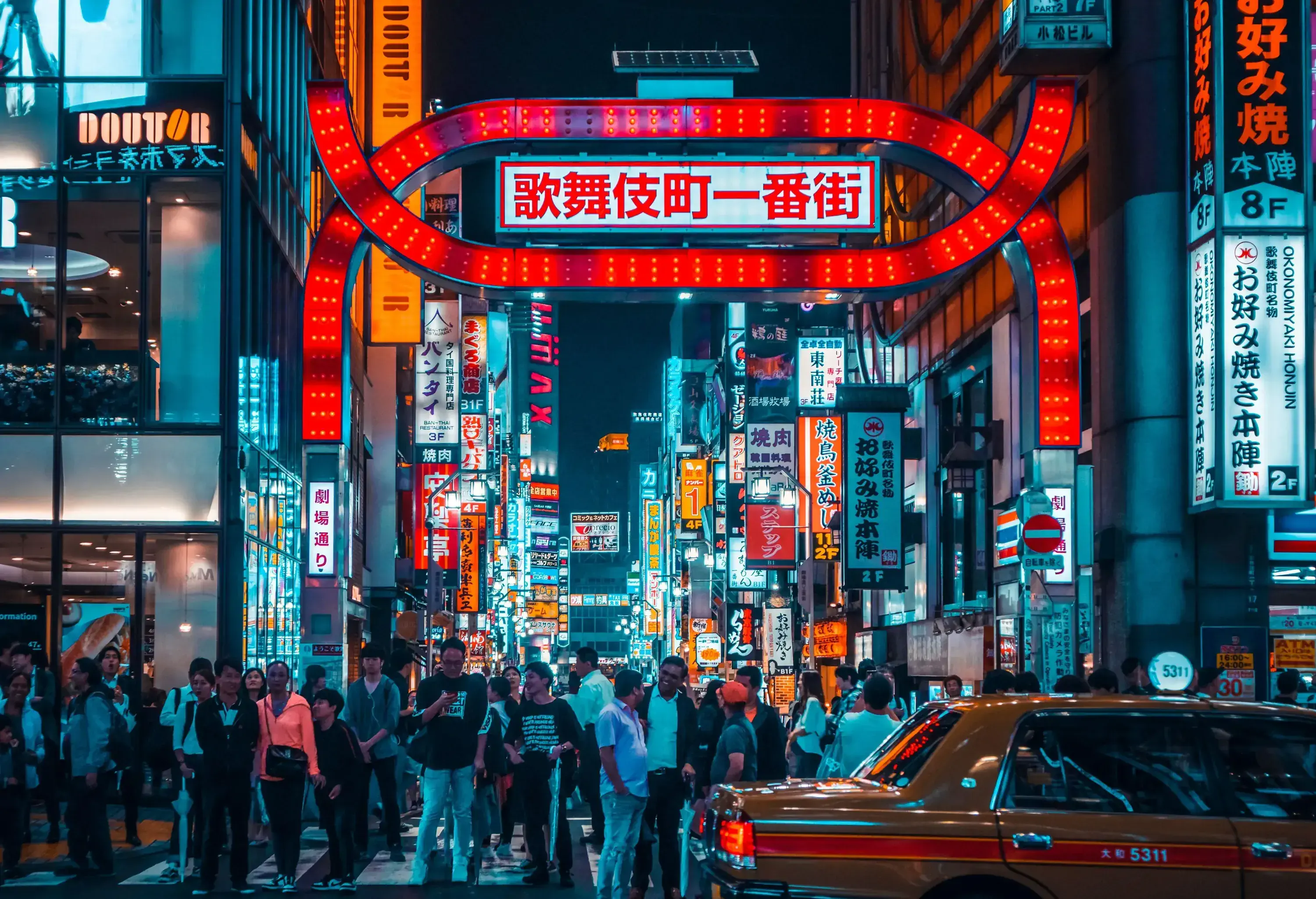 A bustling street is filled with crowds of people and surrounded by an explosion of brightly-lit signs and advertisements.