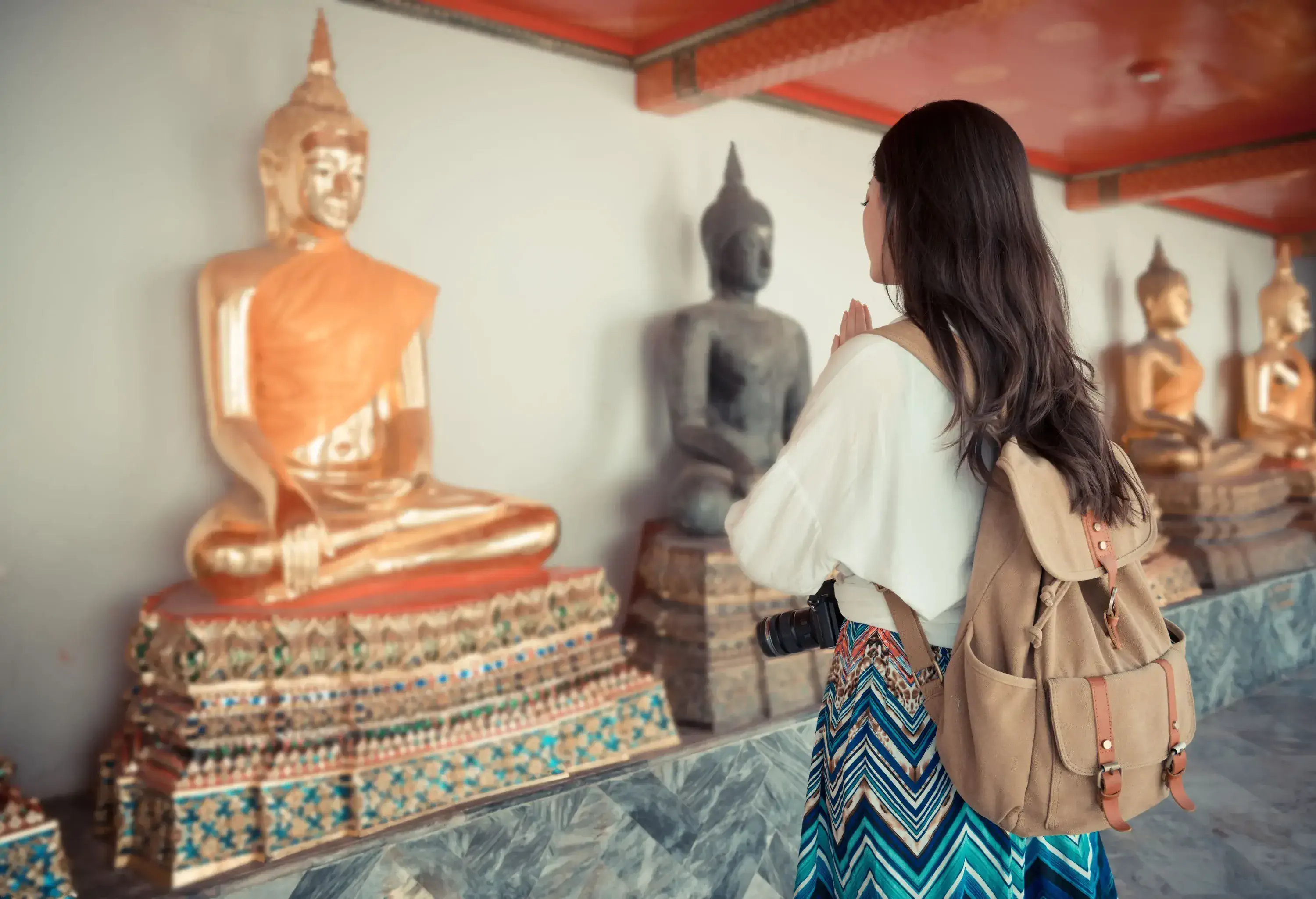 A standing female praying in front of the lined golden Buddha statues.