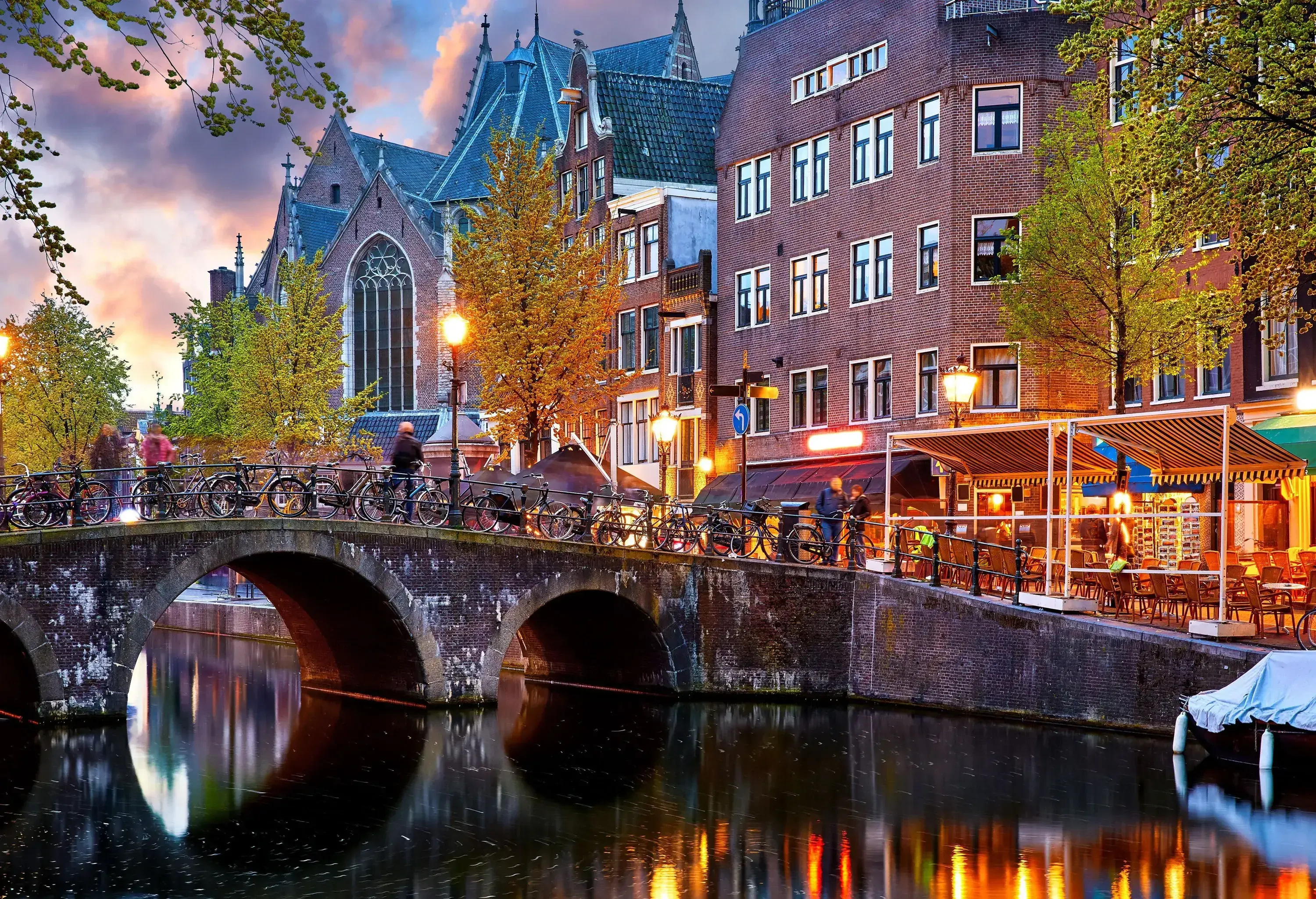An arch bridge over a river with outdoor cafes and lofty historic buildings along the banks.