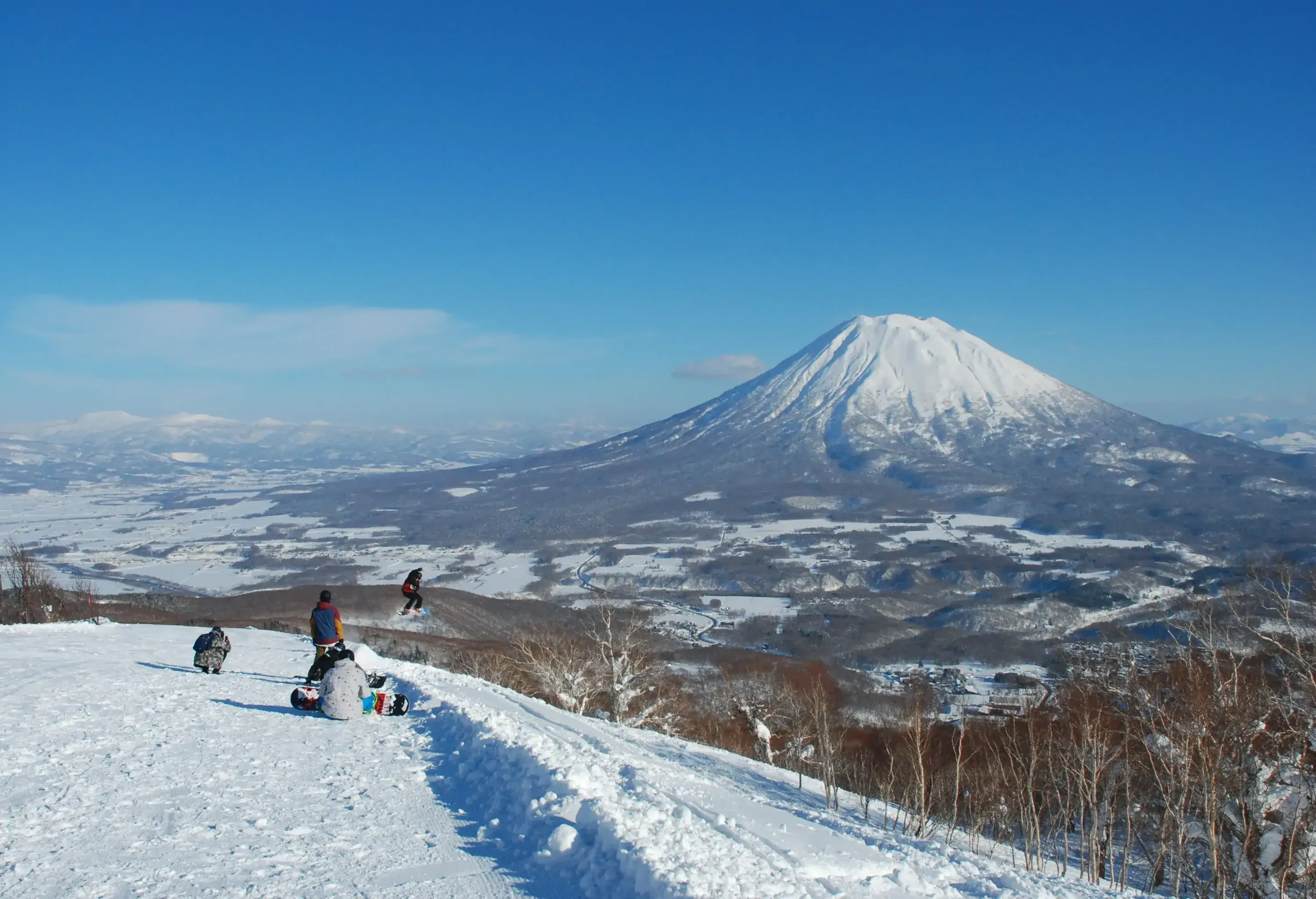Snowboarders resting and performing tricks on a snow hill while a snow-capped mountain serves as their backdrop.