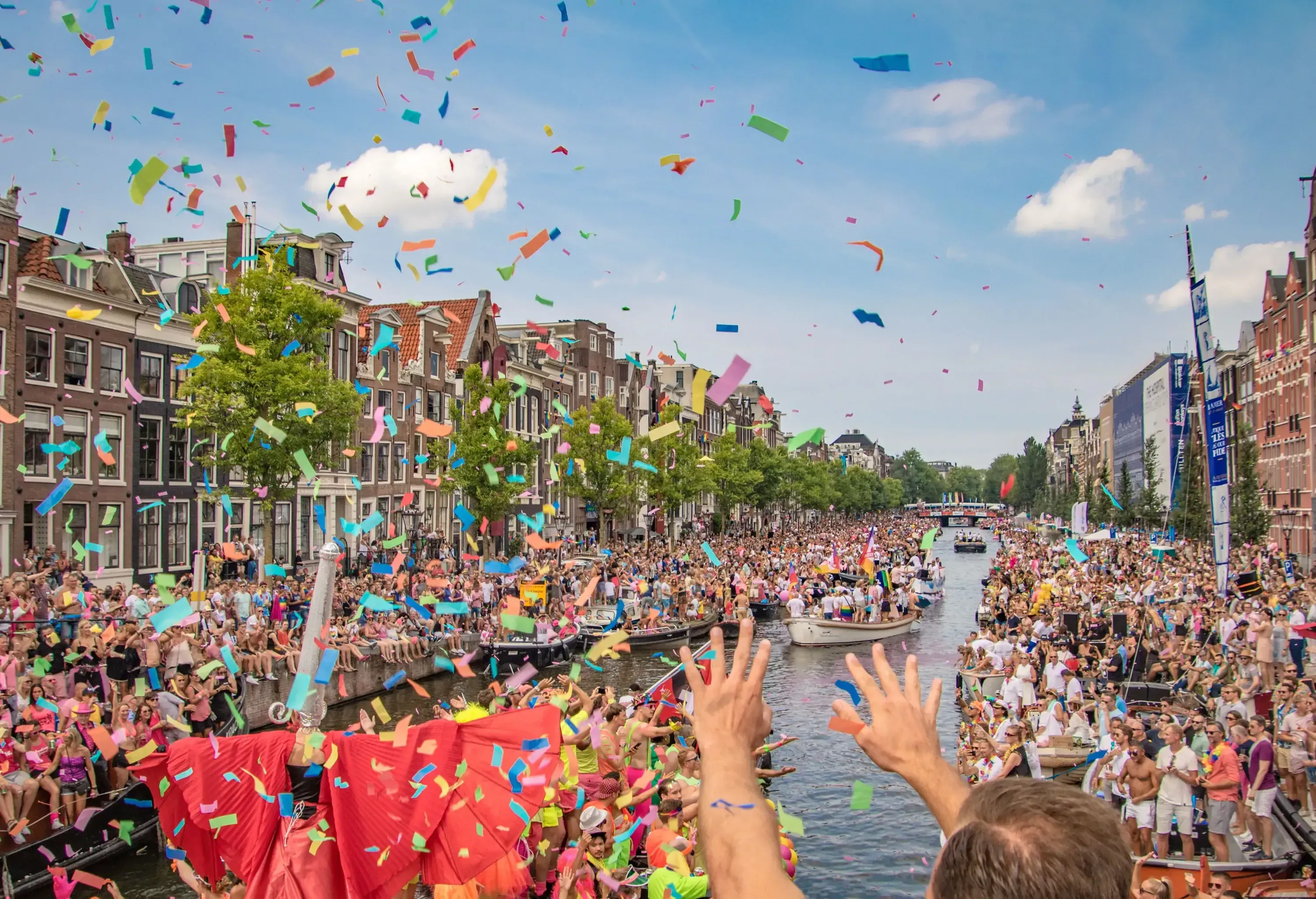 A shower of confetti over a canal parade with boats and banks packed with people.