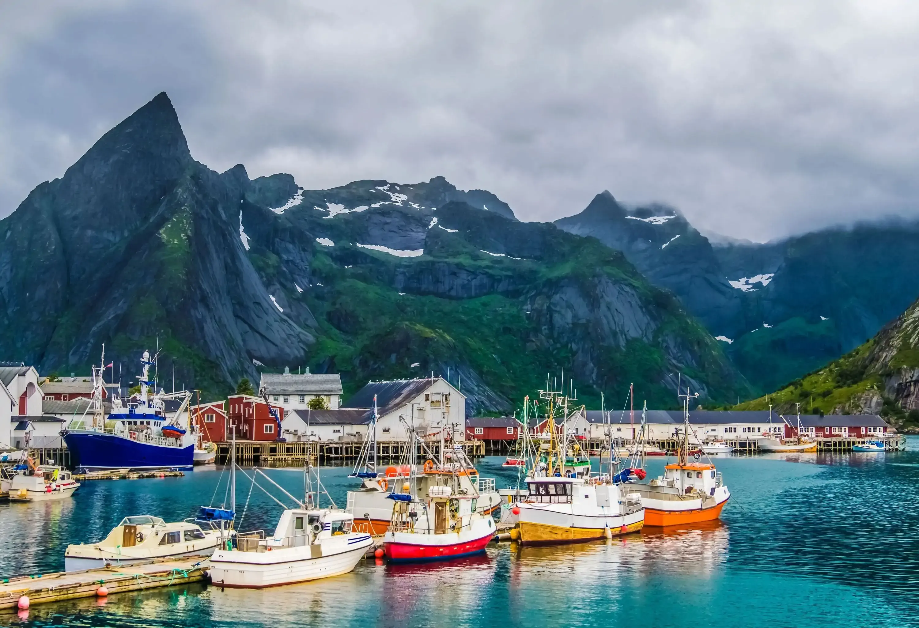 A fishing village with boats and houses along the docks backdropped by rugged mountains.