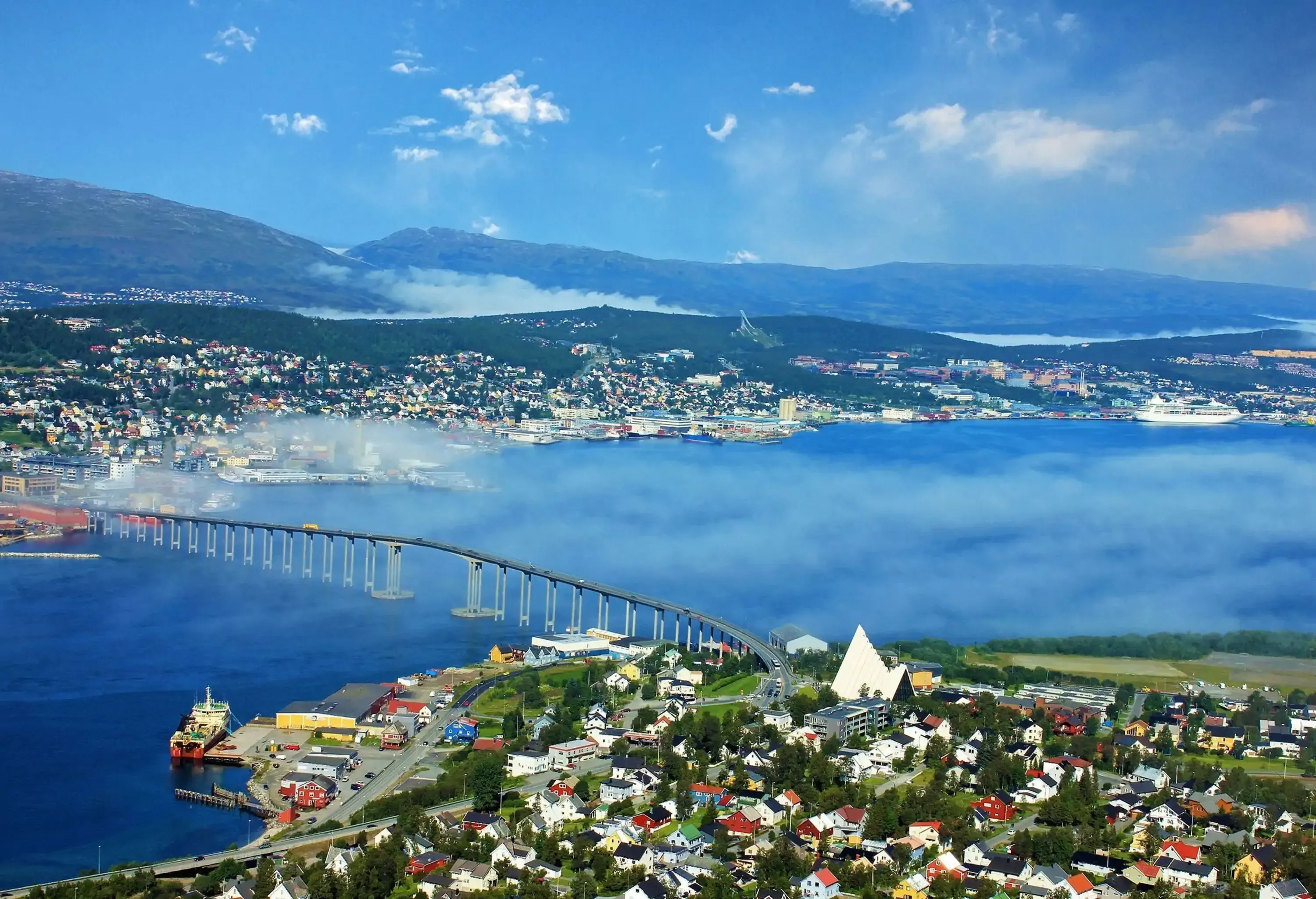 A bridge across a foggy fjord connects two residential neighbourhoods in a city.